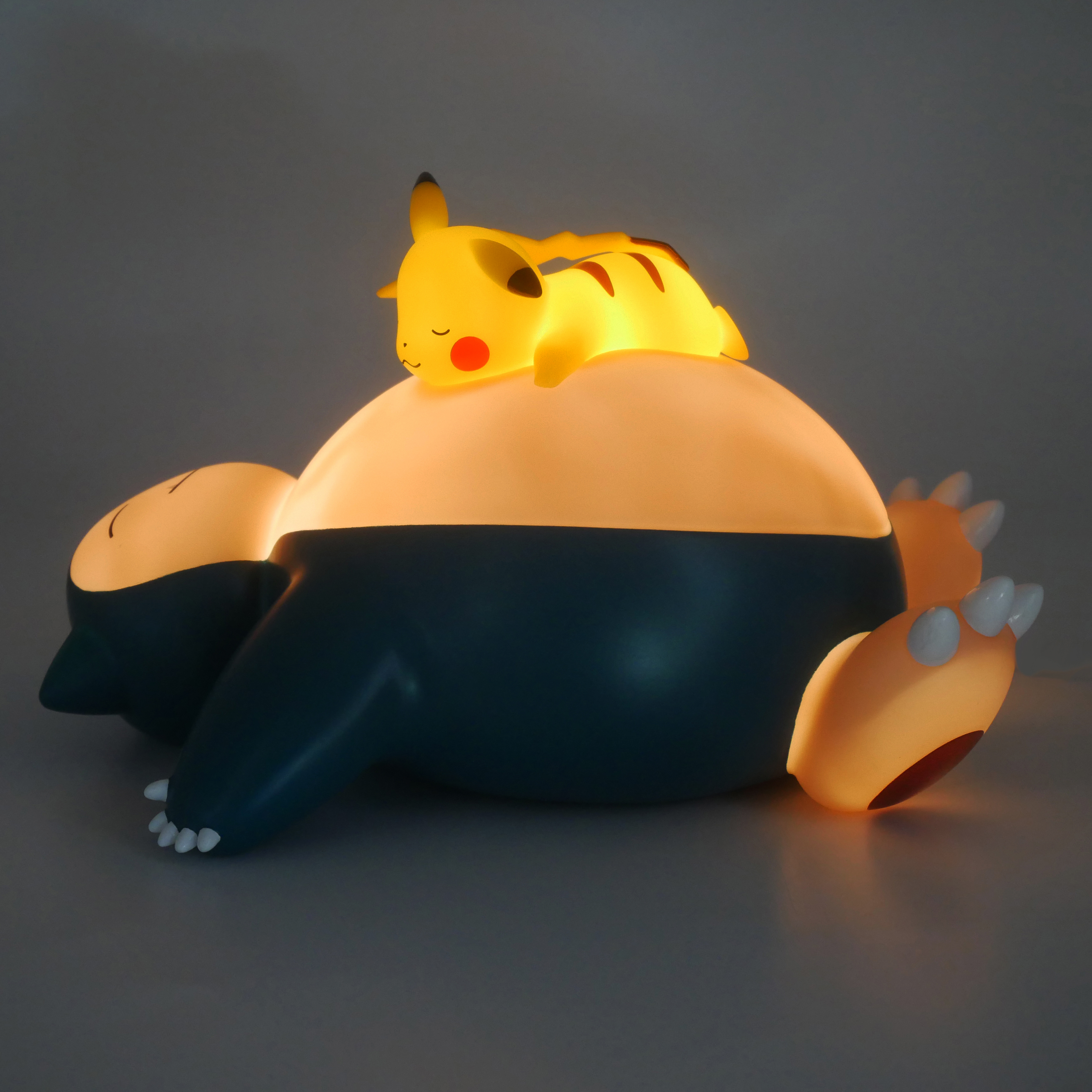 Lampada Snorlax con Pikachu sopra, illuminata in una stanza buia, creando una luce calda.