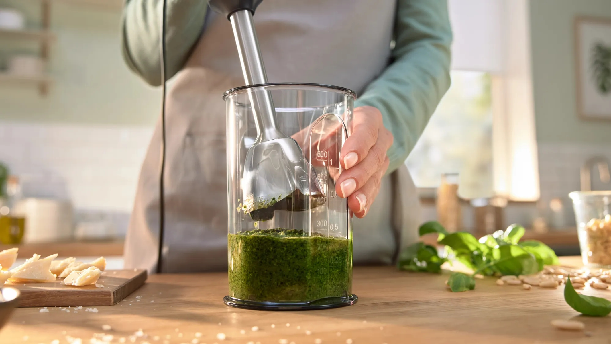 Osoba miksująca pesto blenderem zanurzeniowym w przezroczystym szklanym pojemniku.