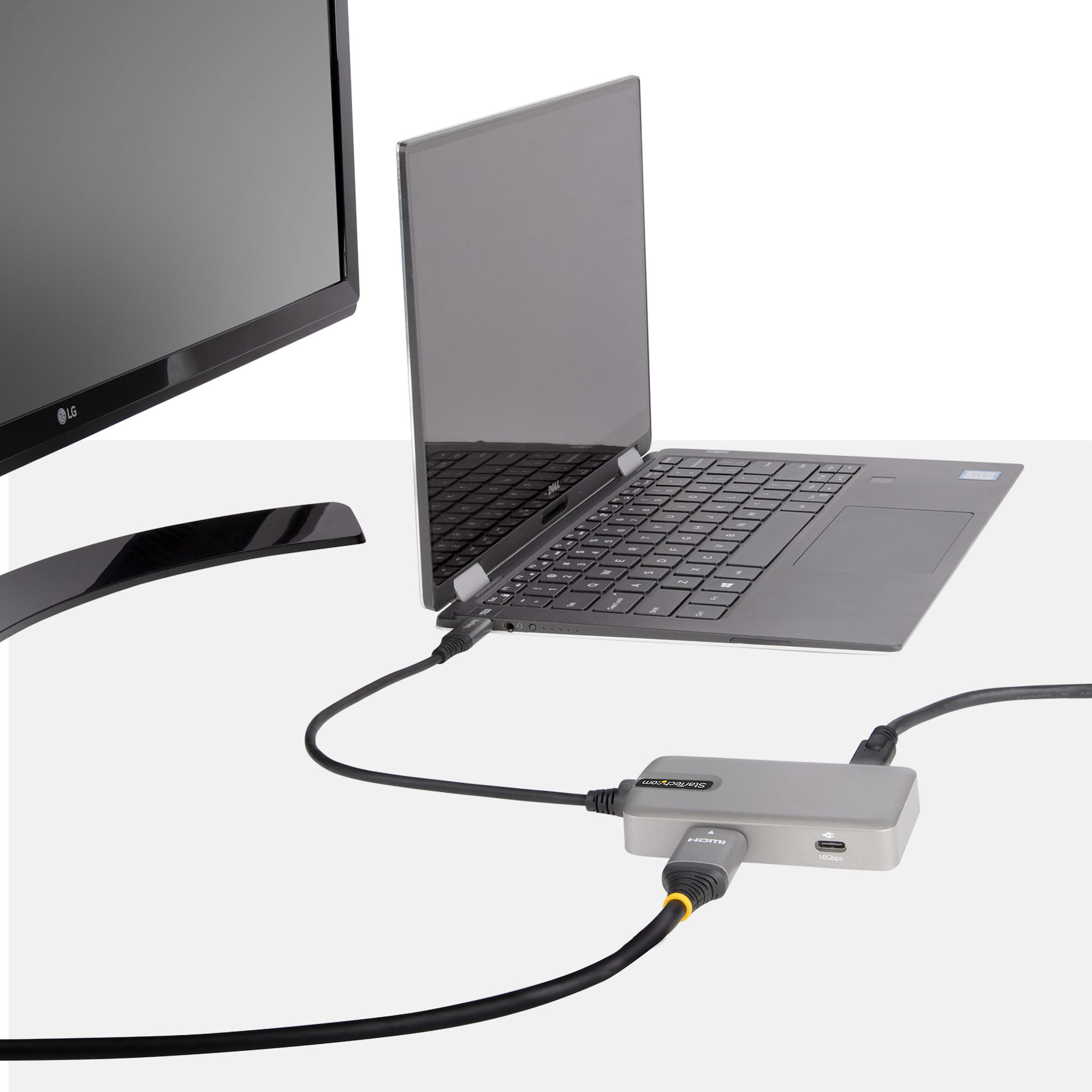 Portátil conectado a monitor y concentrador. Cables negros y un concentrador gris sobre la superficie blanca.