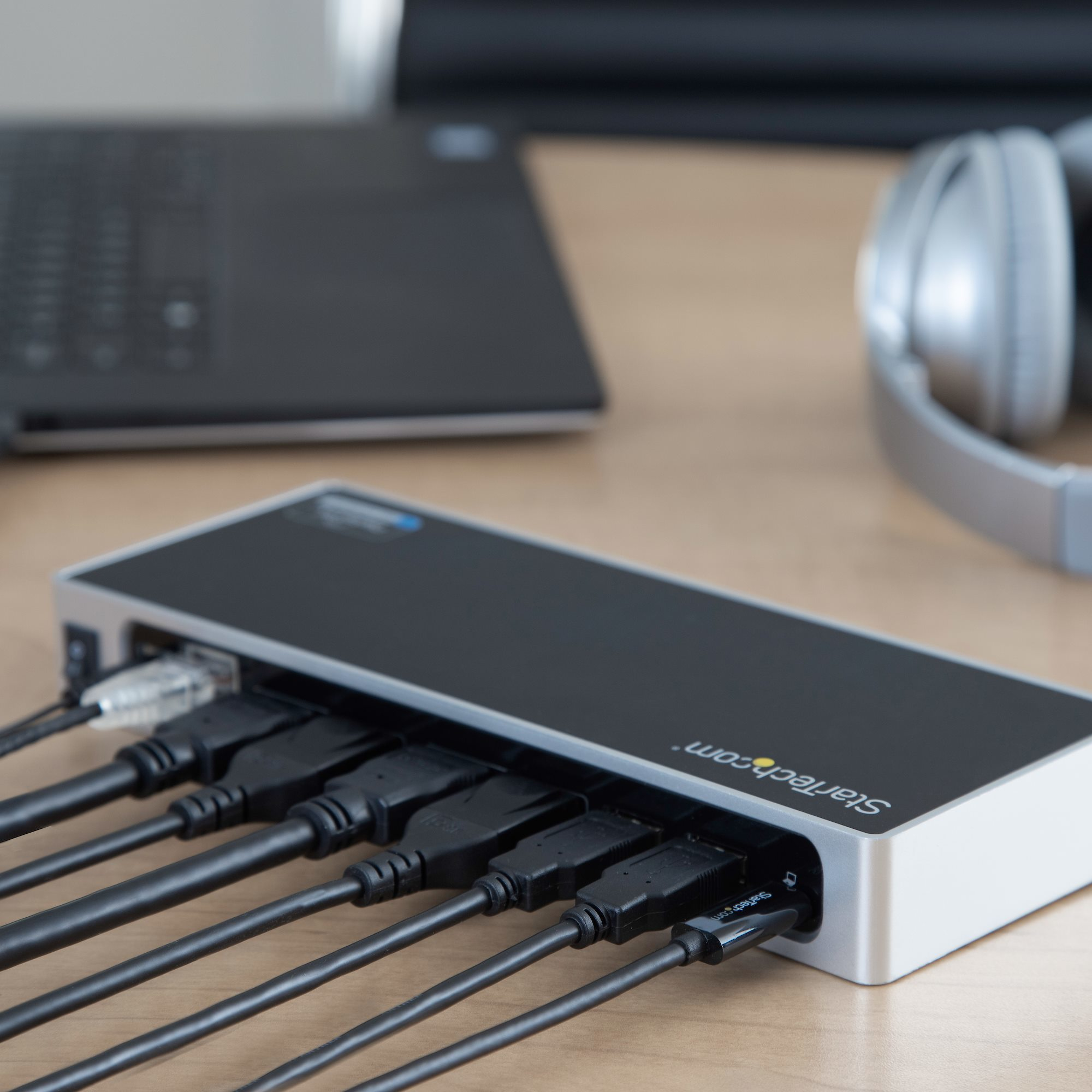 Base de conexión StarTech.com con múltiples puertos y cables conectados en escritorio de madera.
