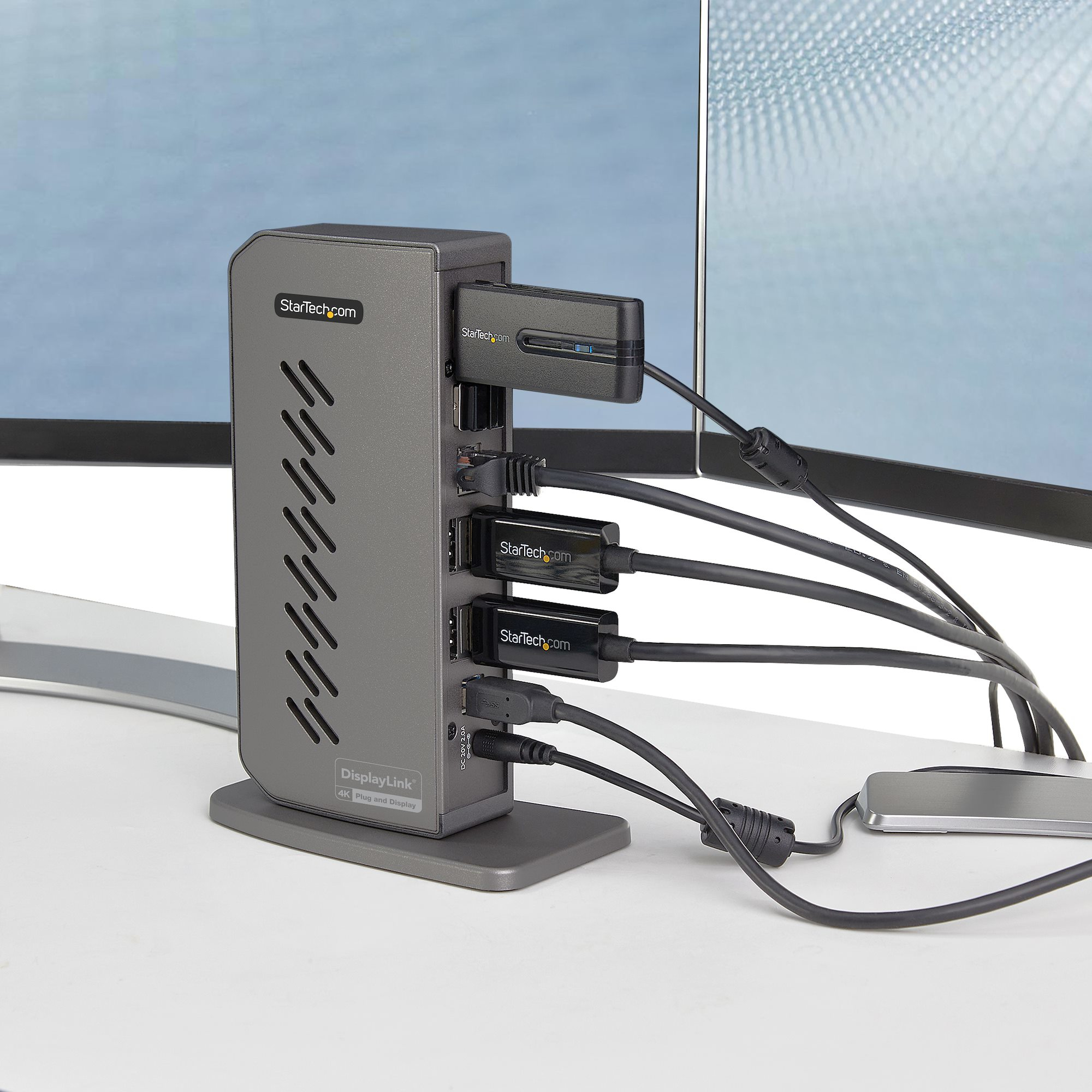 Una docking station grigia con più porte e cavi collegati, su una scrivania bianca.