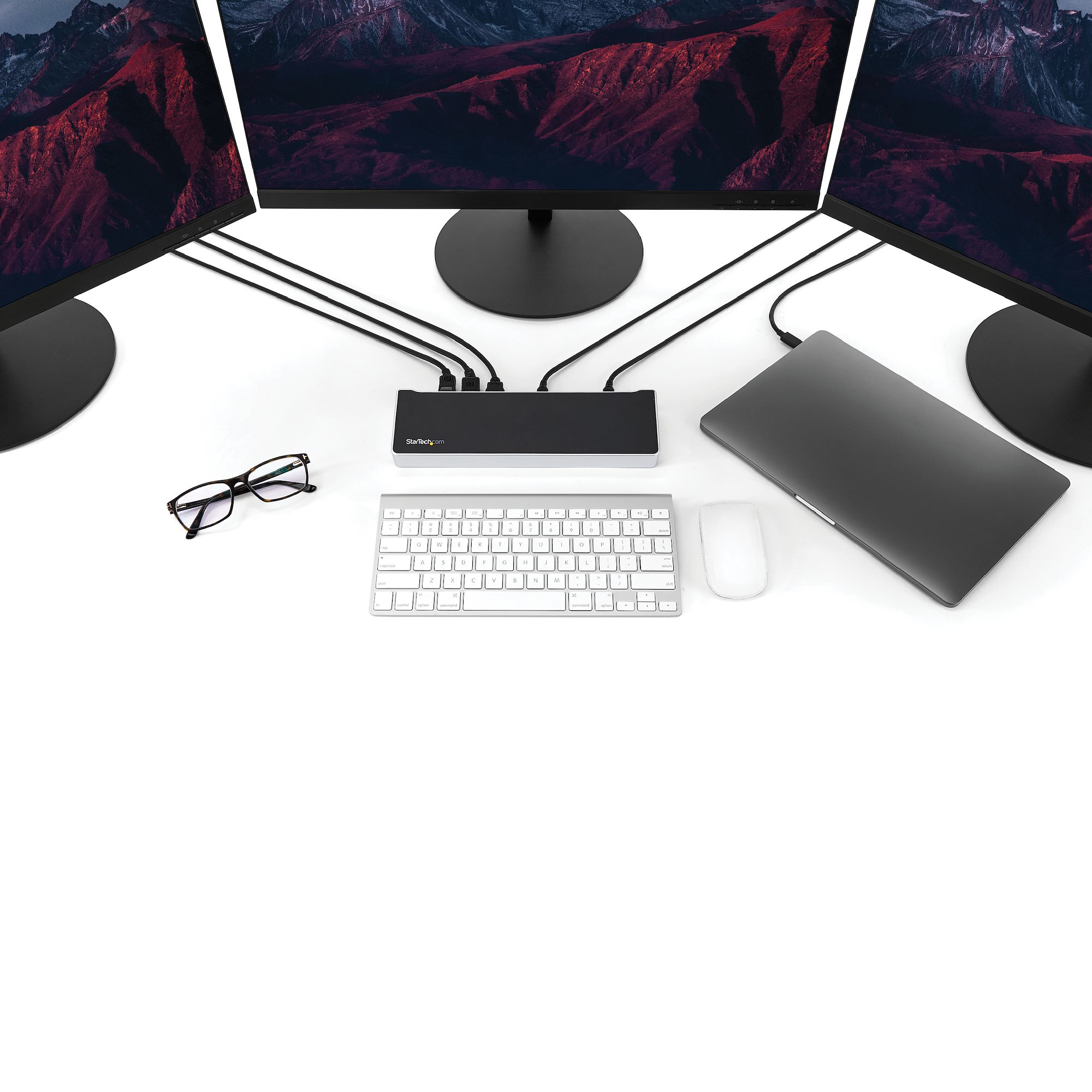 Spazio di lavoro con tre monitor, laptop, tastiera, mouse e docking station.