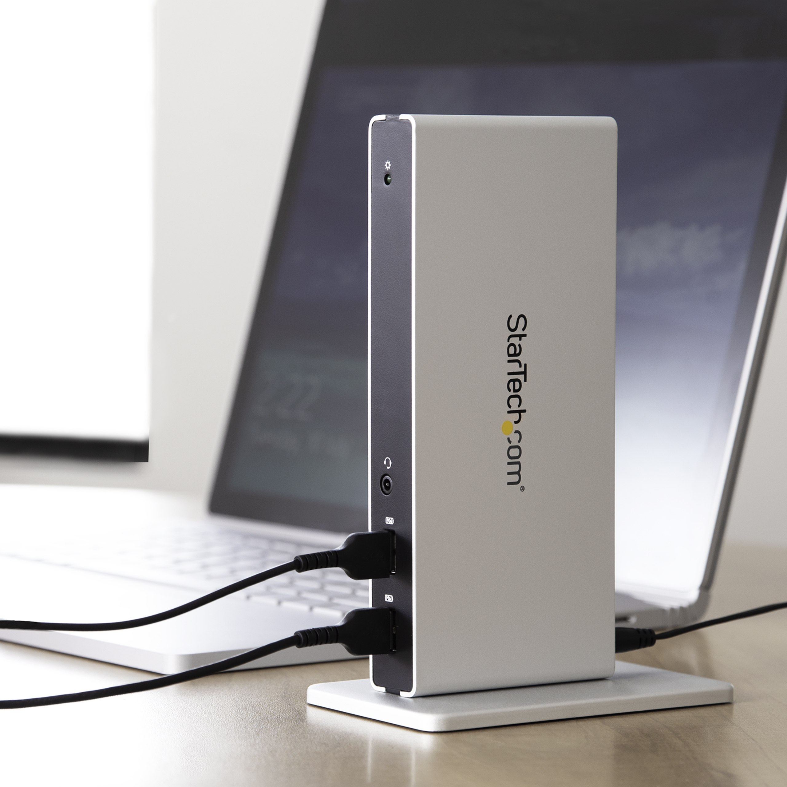 Docking station argentata con porte, collegata a un laptop. Il logo StarTech.com è visibile.