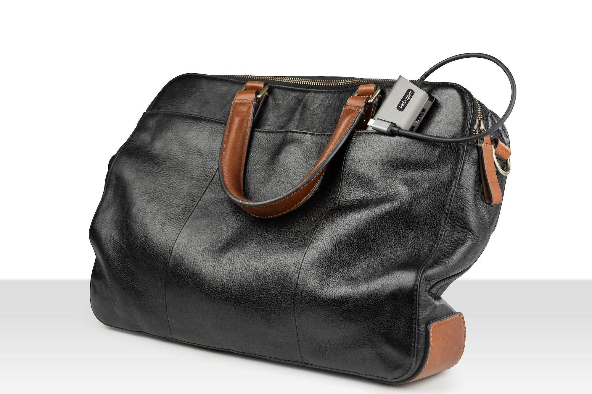 Bolso de cuero negro con un dispositivo plateado sobresaliendo. Asas y ribetes de cuero marrón.