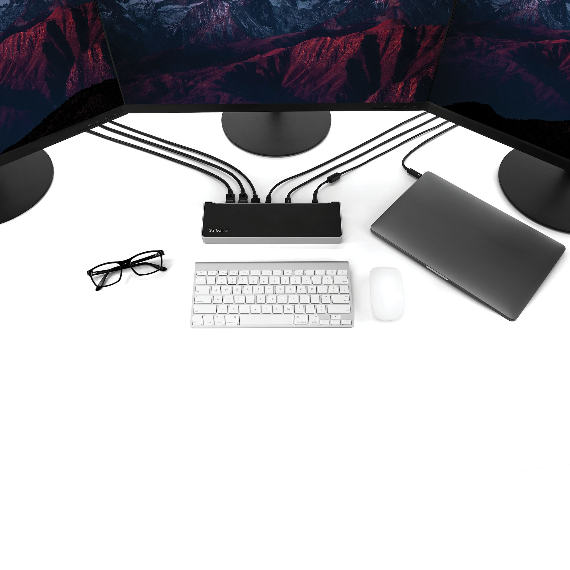 Un portátil, teclado, ratón y concentrador USB sobre una superficie blanca.