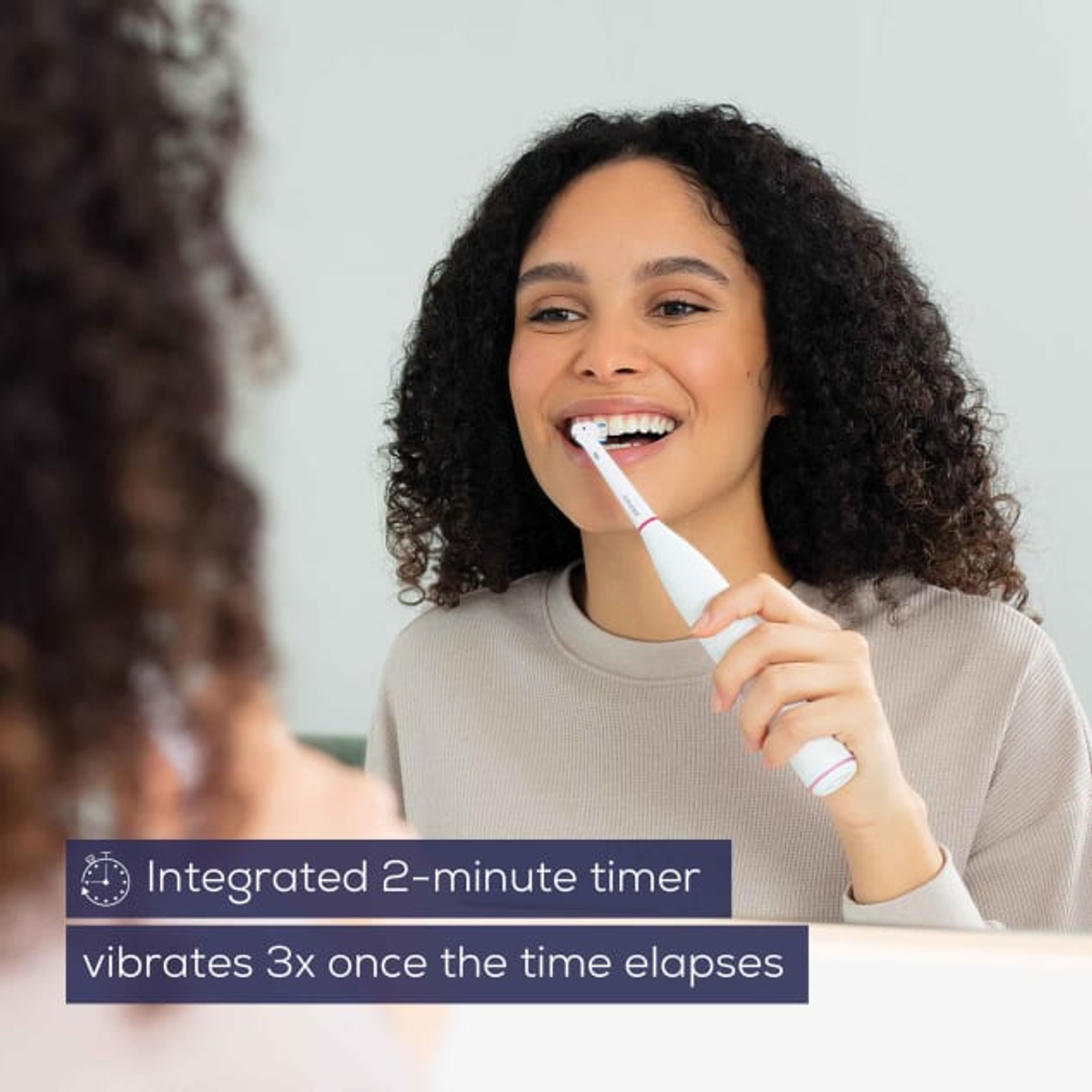 Una mujer cepillándose los dientes con un cepillo eléctrico, mirándose al espejo.