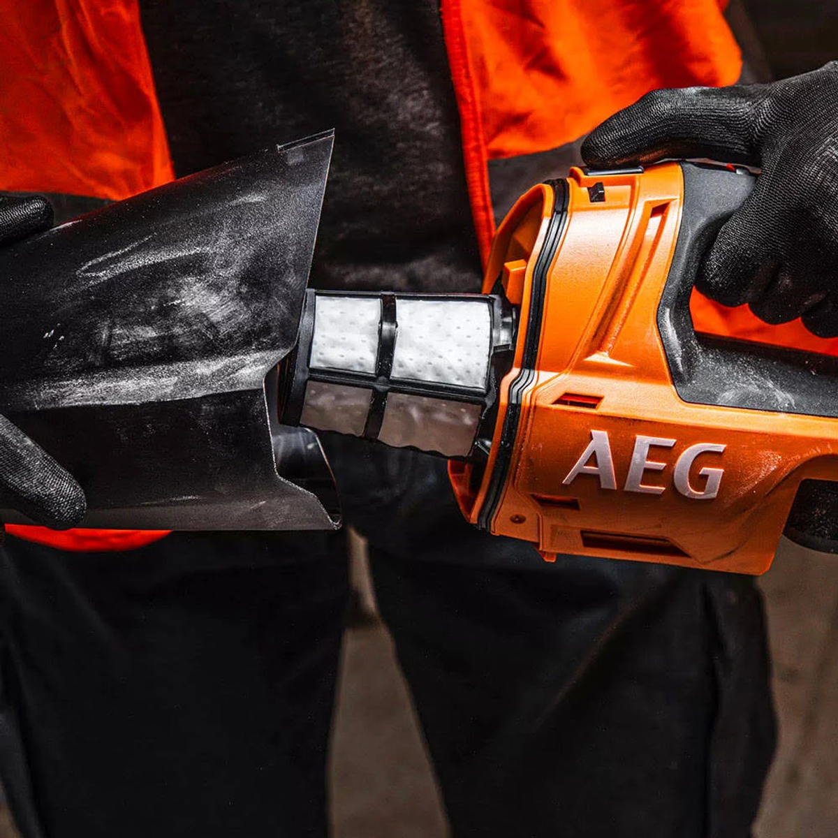 Un utensile AEG arancione con un filtro rimosso da mani guantate. I colori dominanti sono il nero e l'arancione.