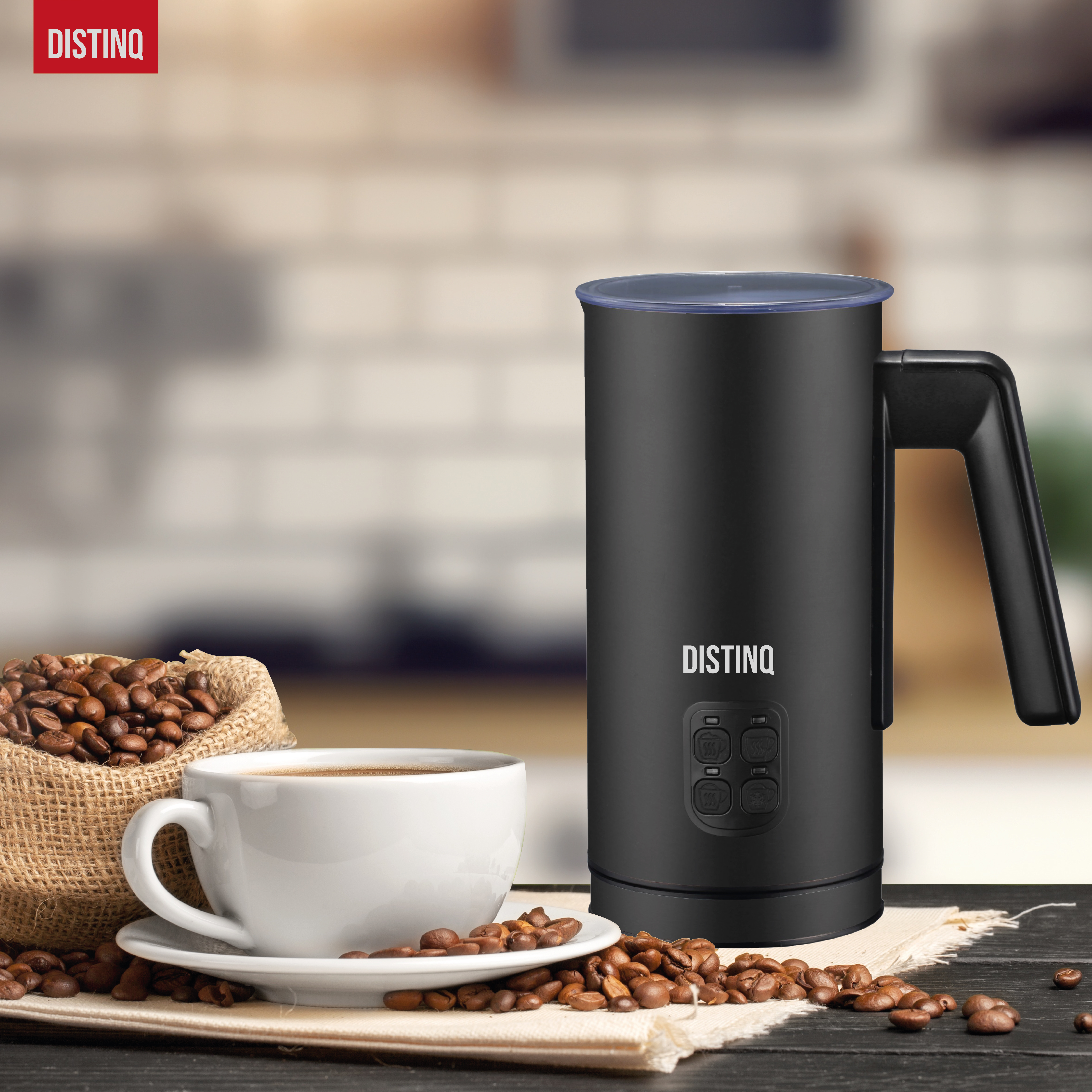 A black milk frother with a cup of coffee and beans on a table. The Distinq logo is visible.
