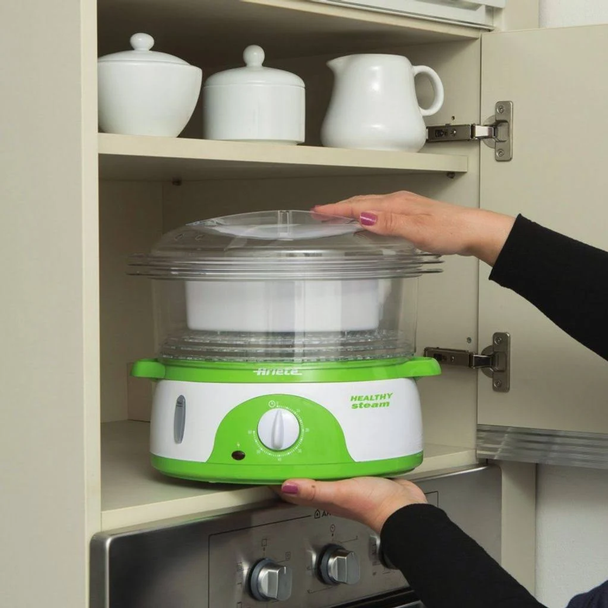 Una persona colocando un vaporizador blanco y verde en un armario sobre un horno.