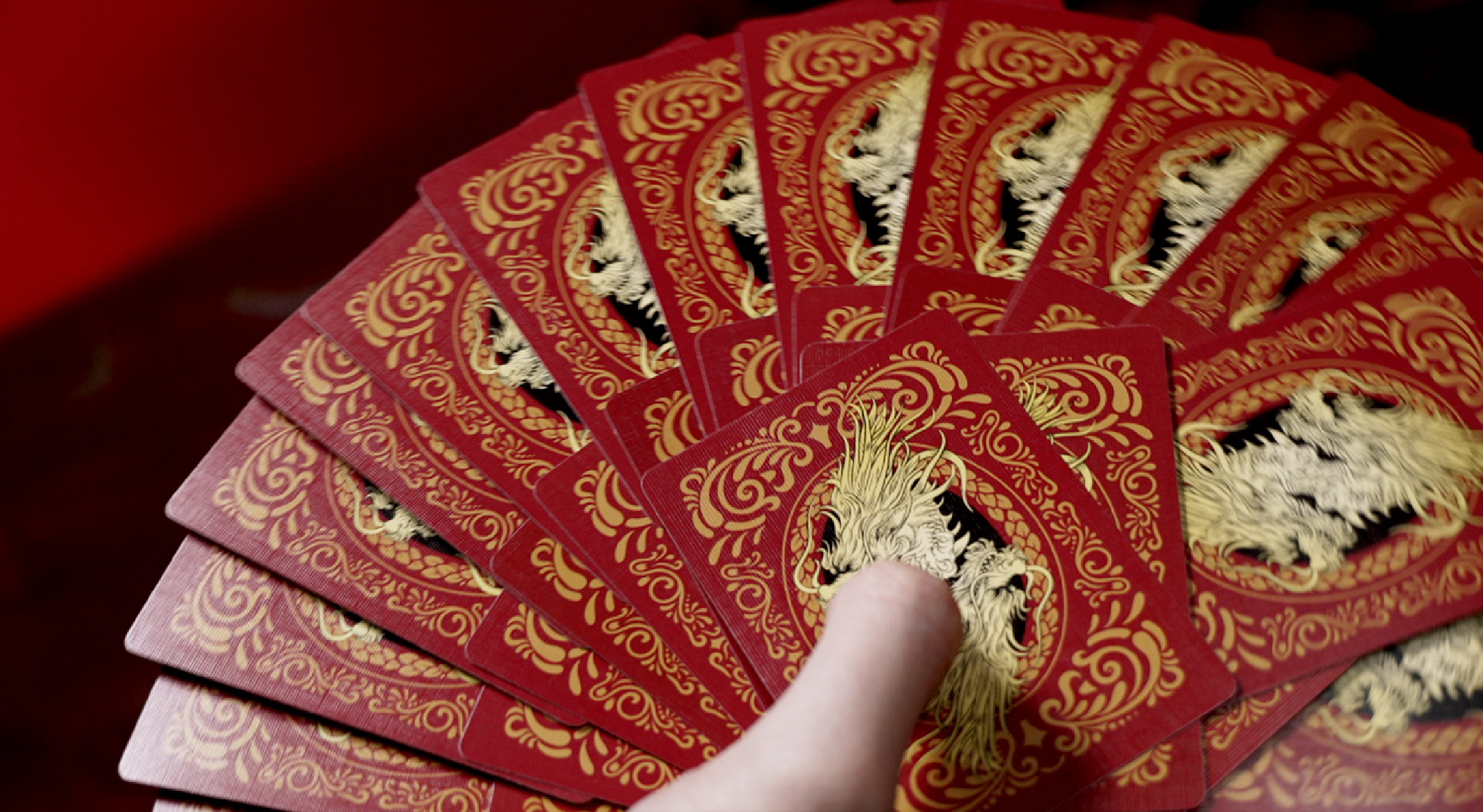 Fächerförmig ausgebreitete Spielkarten, rot-goldenes Design, gehalten von einer Hand, Nahaufnahme.