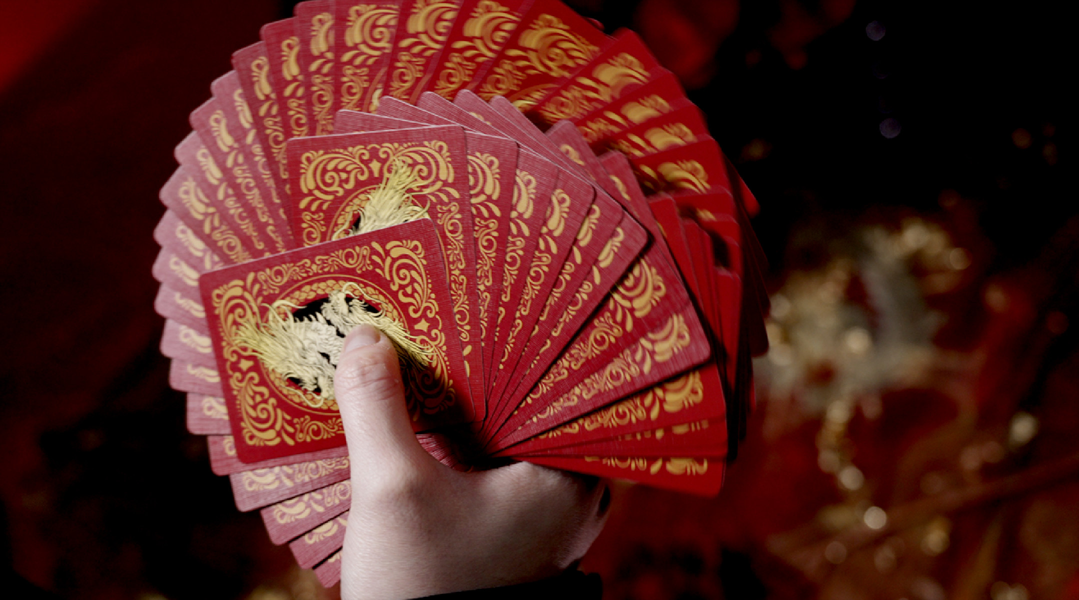 Eine Hand fächert einen Stapel roter Spielkarten mit goldenen Verzierungen auf.