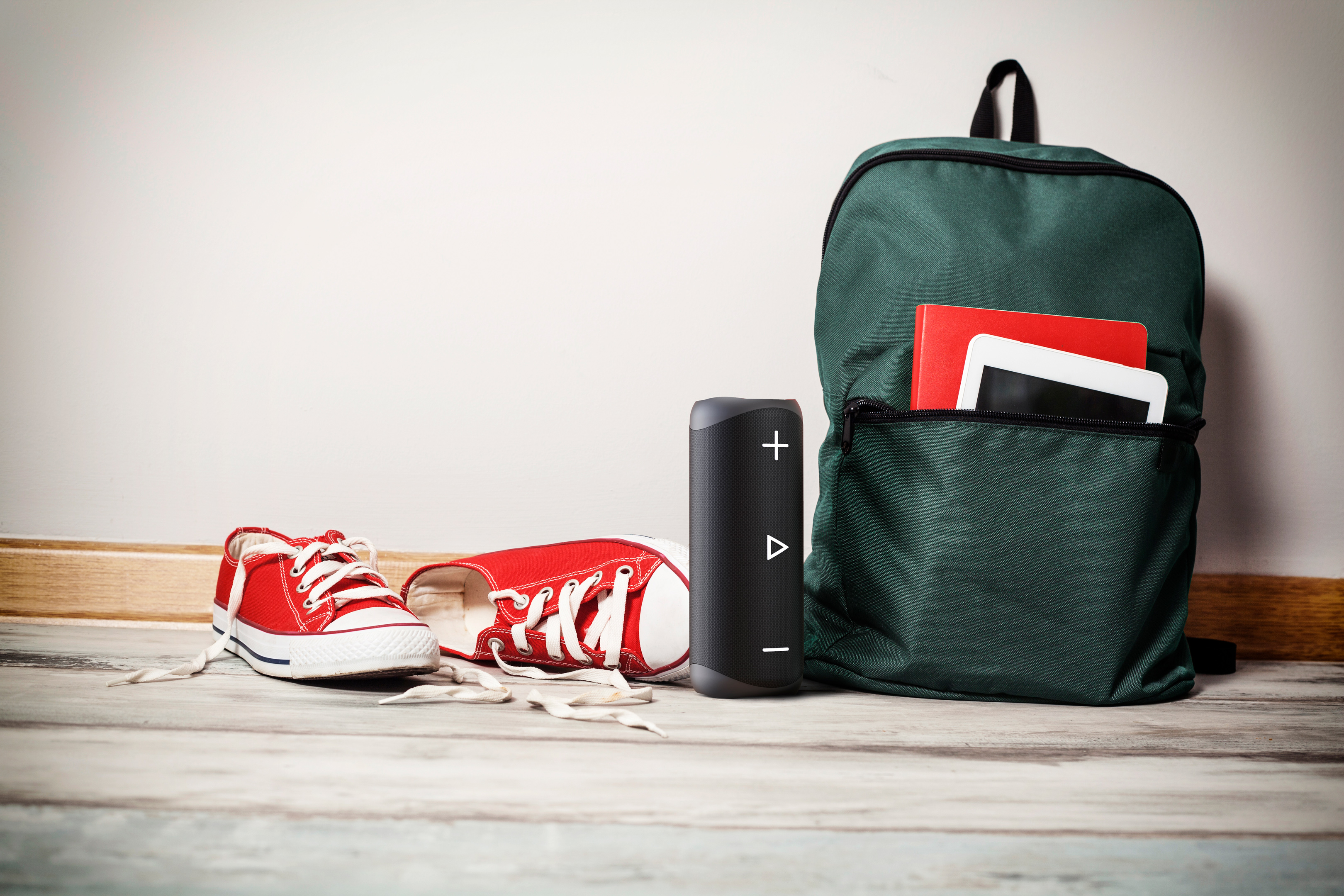 Plecak, czerwone buty, głośnik i tablet na drewnianej podłodze. Biała ściana w tle. Rozrzucone liście.