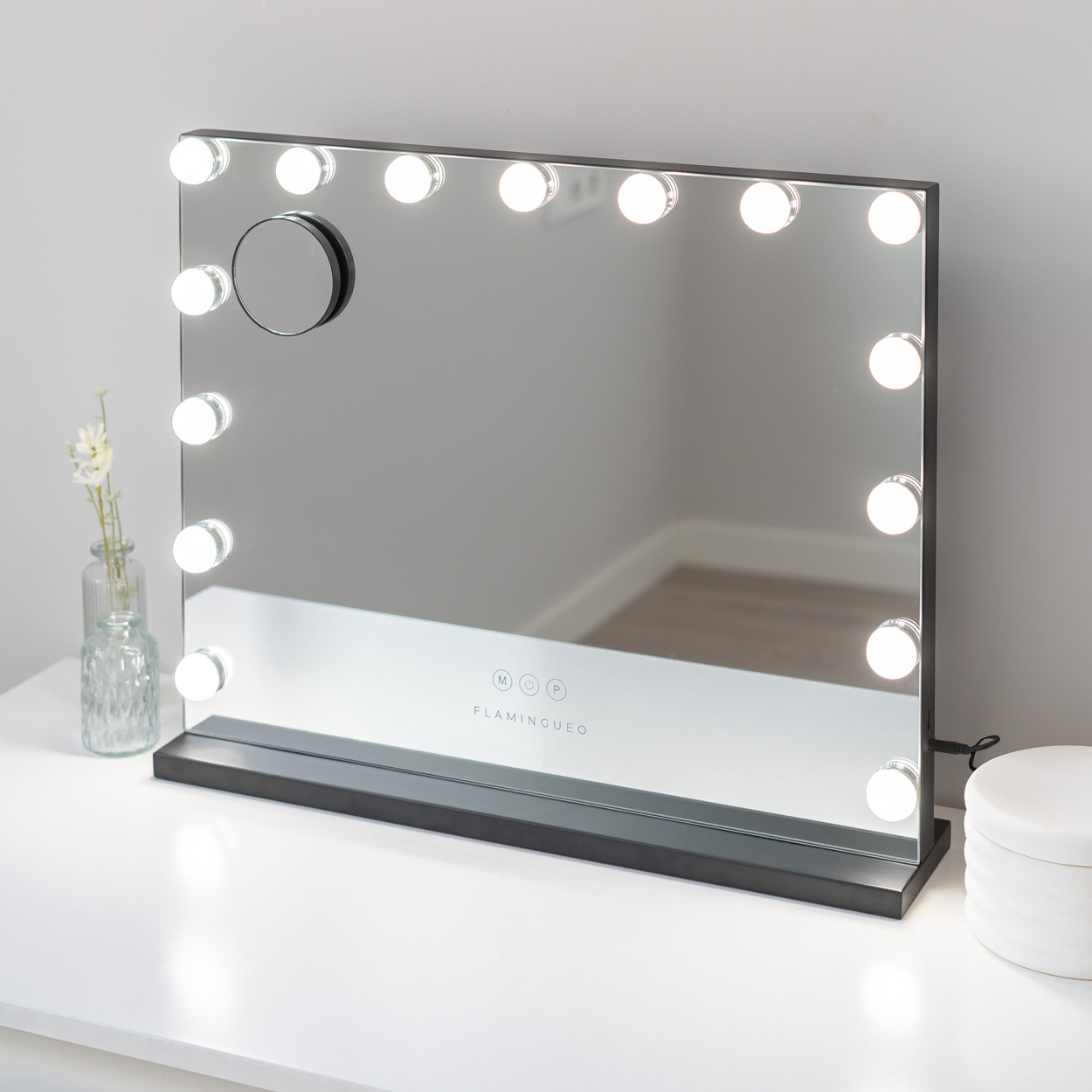 Un espejo de maquillaje iluminado con marco negro sobre una superficie blanca.