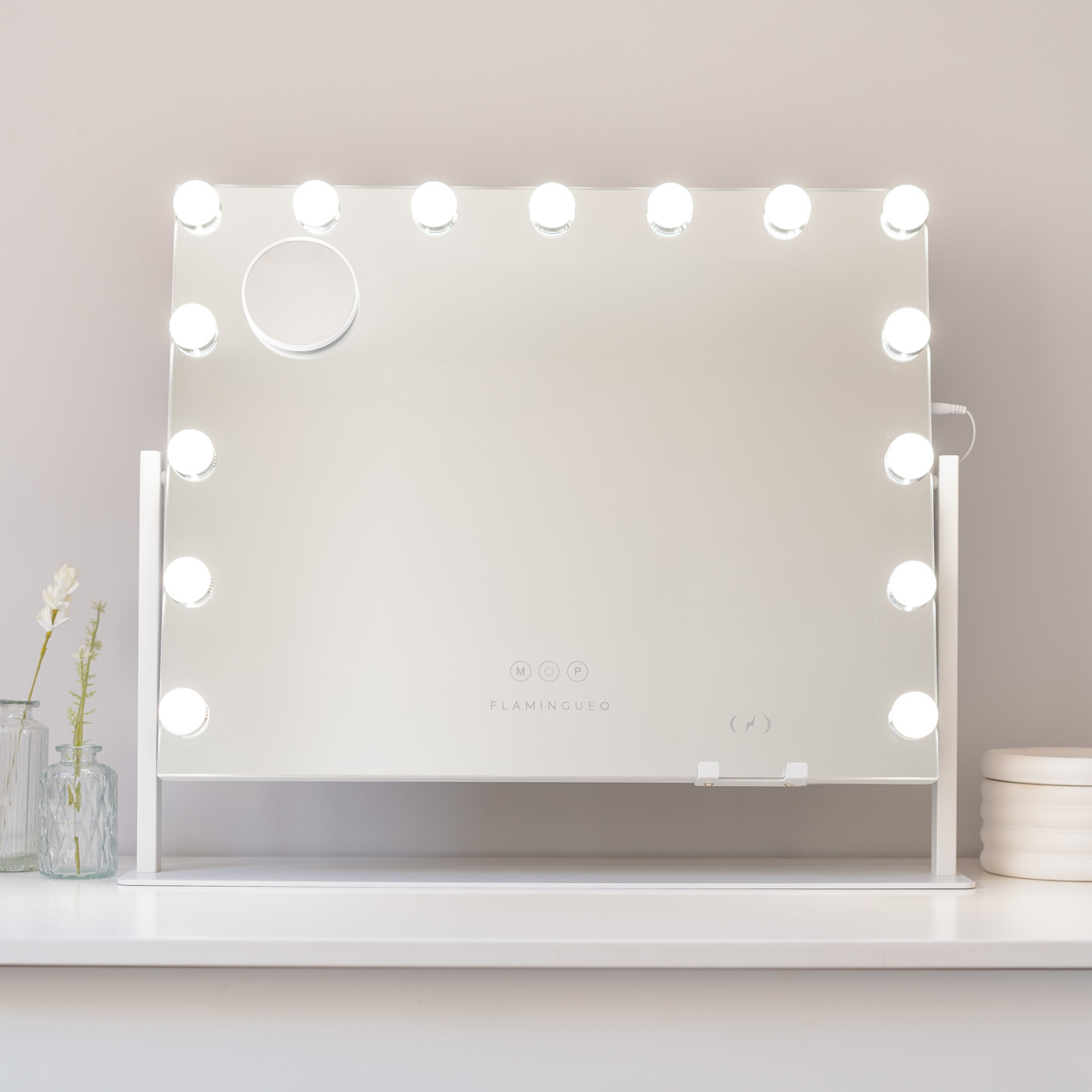 Un espejo de tocador con luces alrededor, un pequeño espejo de aumento y una base blanca.