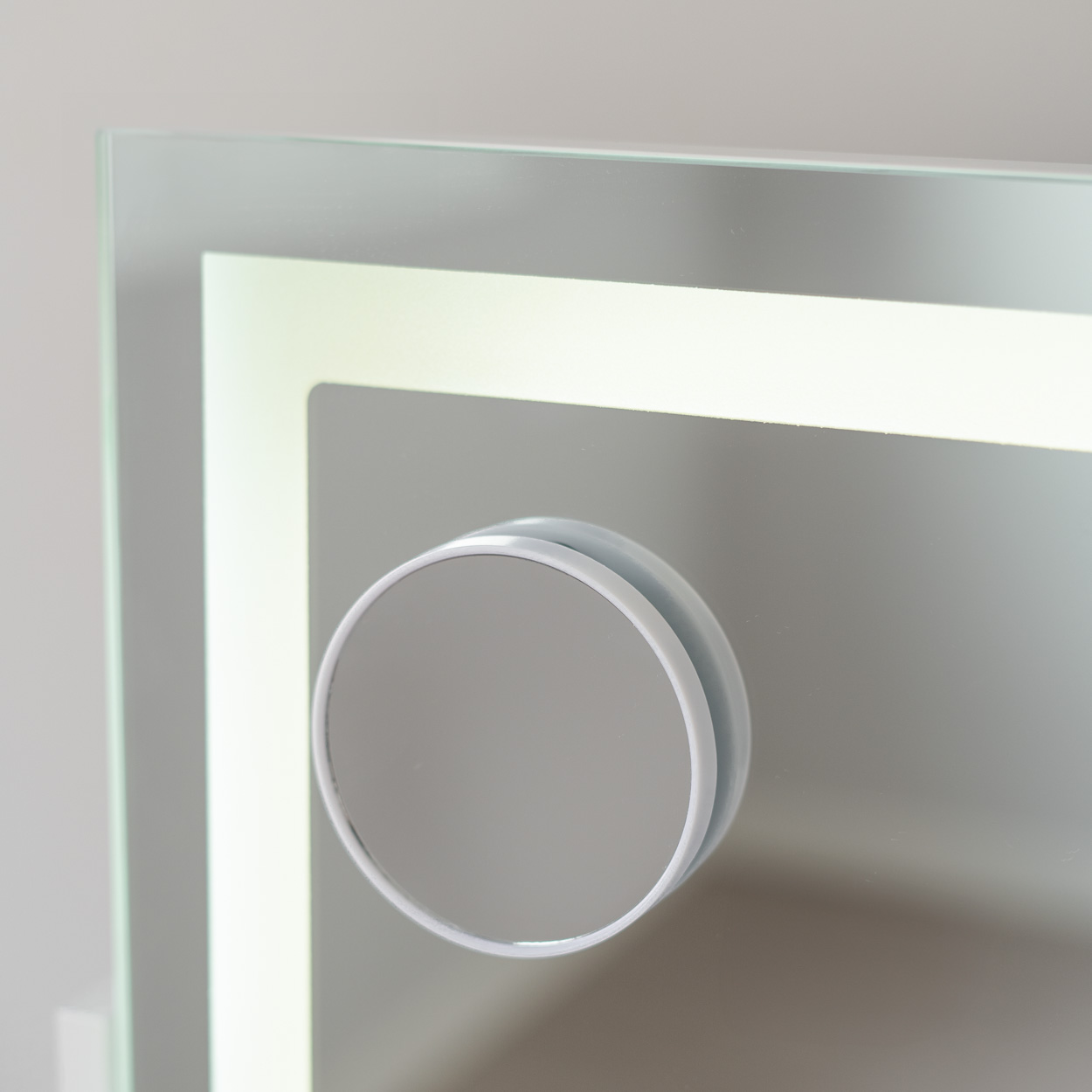 Primer plano de espejo iluminado con un pequeño espejo circular adjunto, sobre un fondo gris claro.
