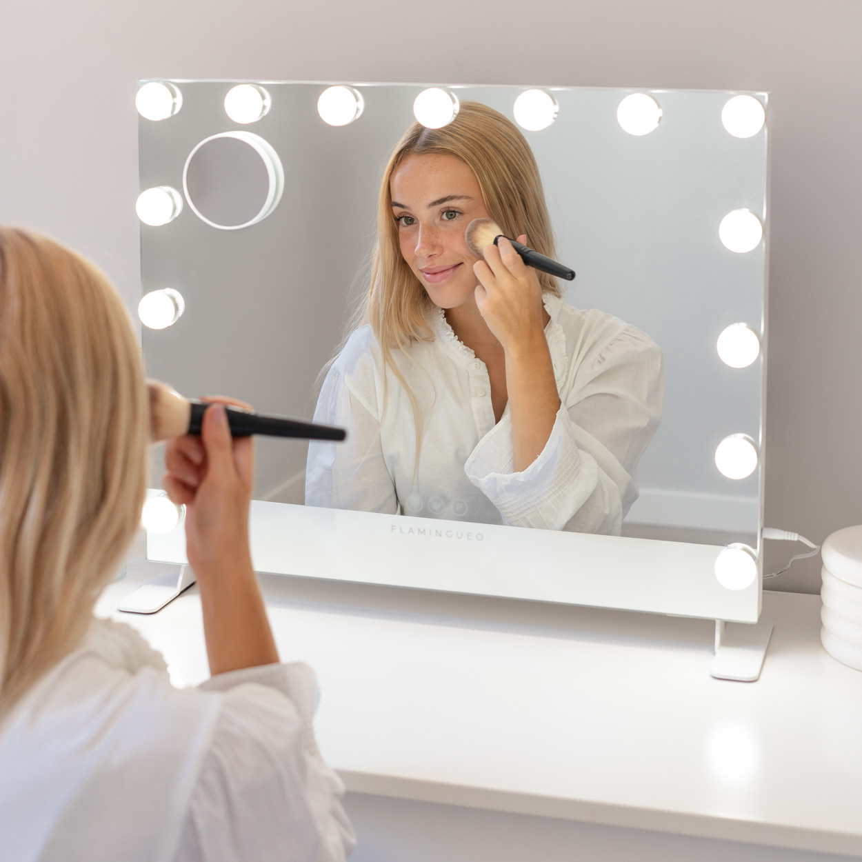 Mujer maquillándose frente a un espejo de maquillaje iluminado.