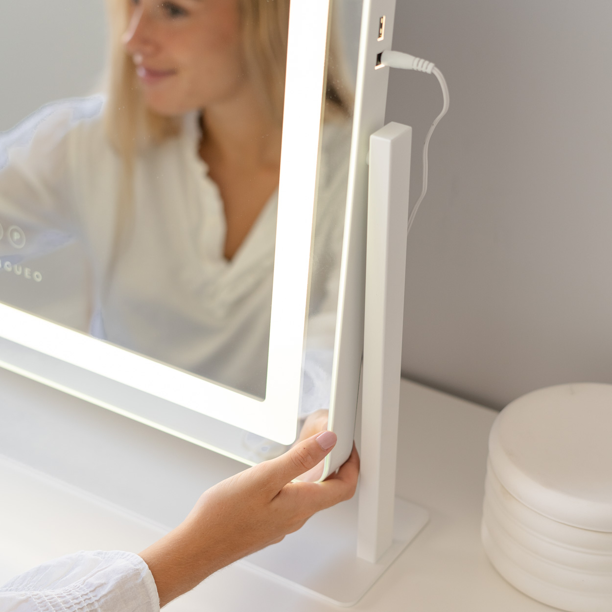 Mujer tocando espejo blanco iluminado con soporte blanco y cable USB.