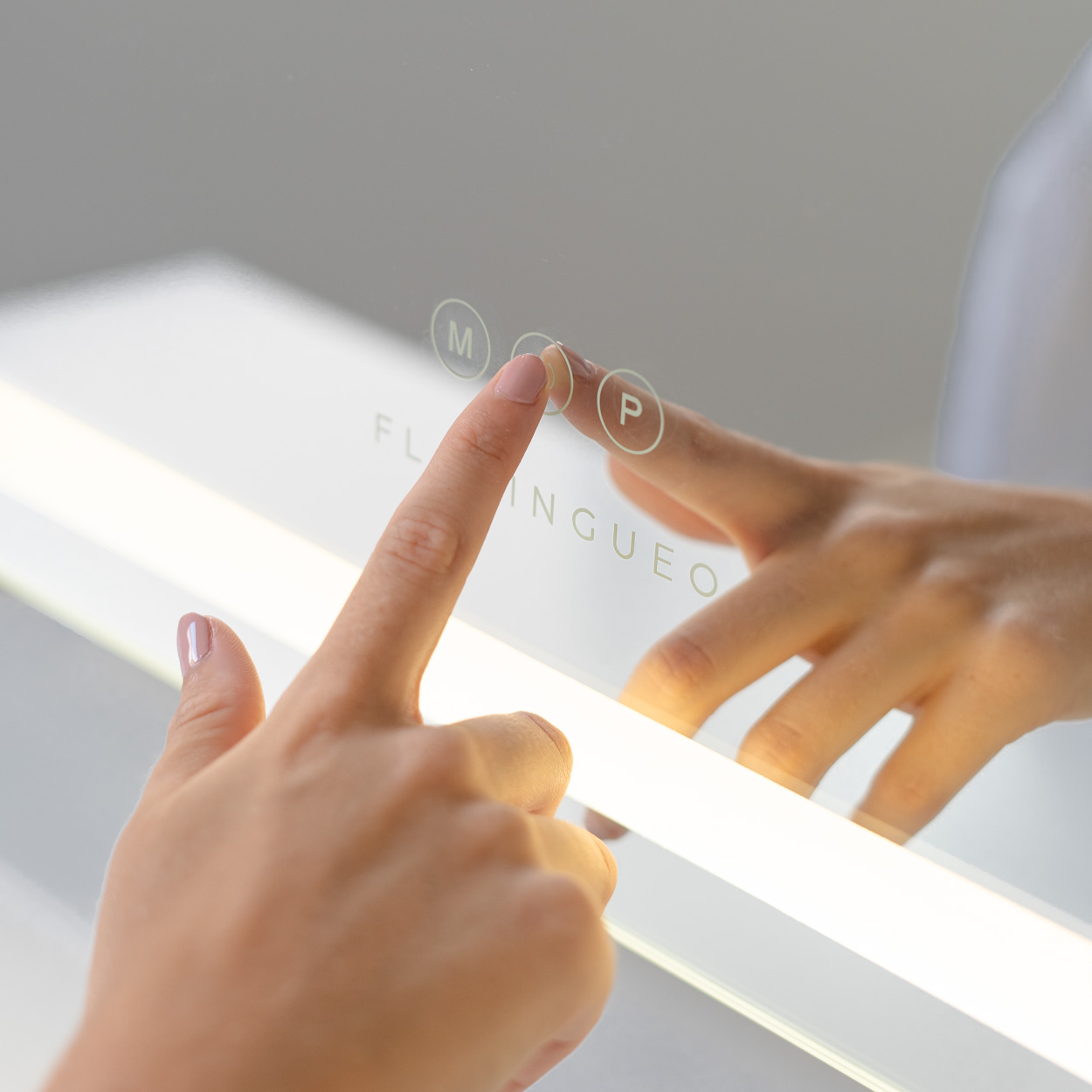 Una mano toca una superficie de espejo con botones táctiles. El espejo refleja la mano.