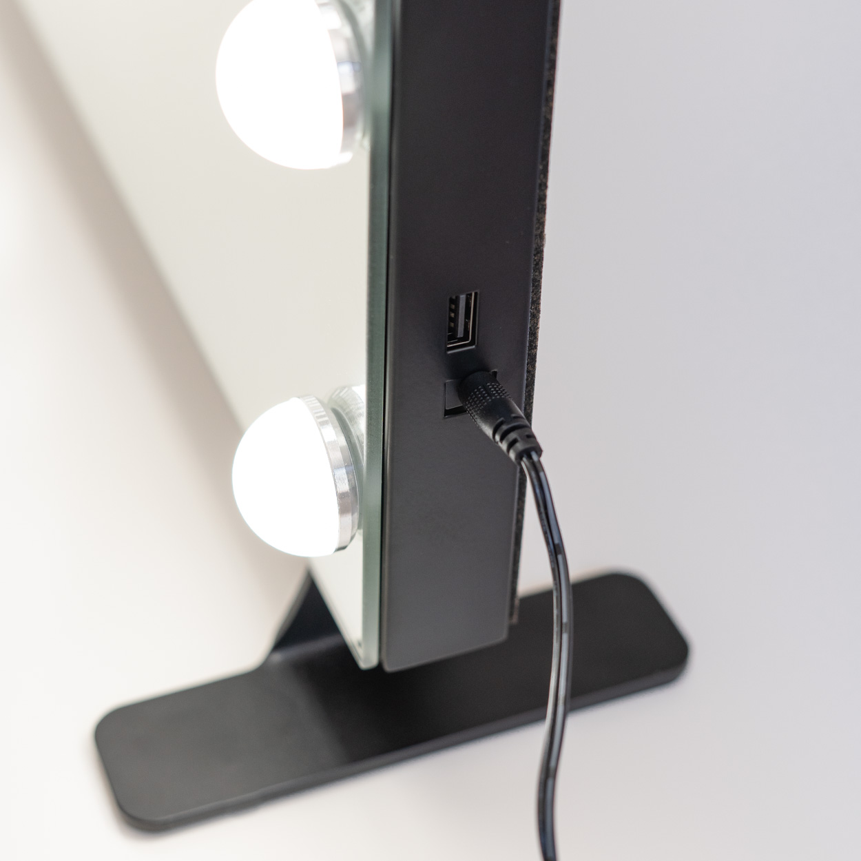 Primer plano de un espejo de maquillaje con luces. Marco negro, puerto de carga y cable negro.