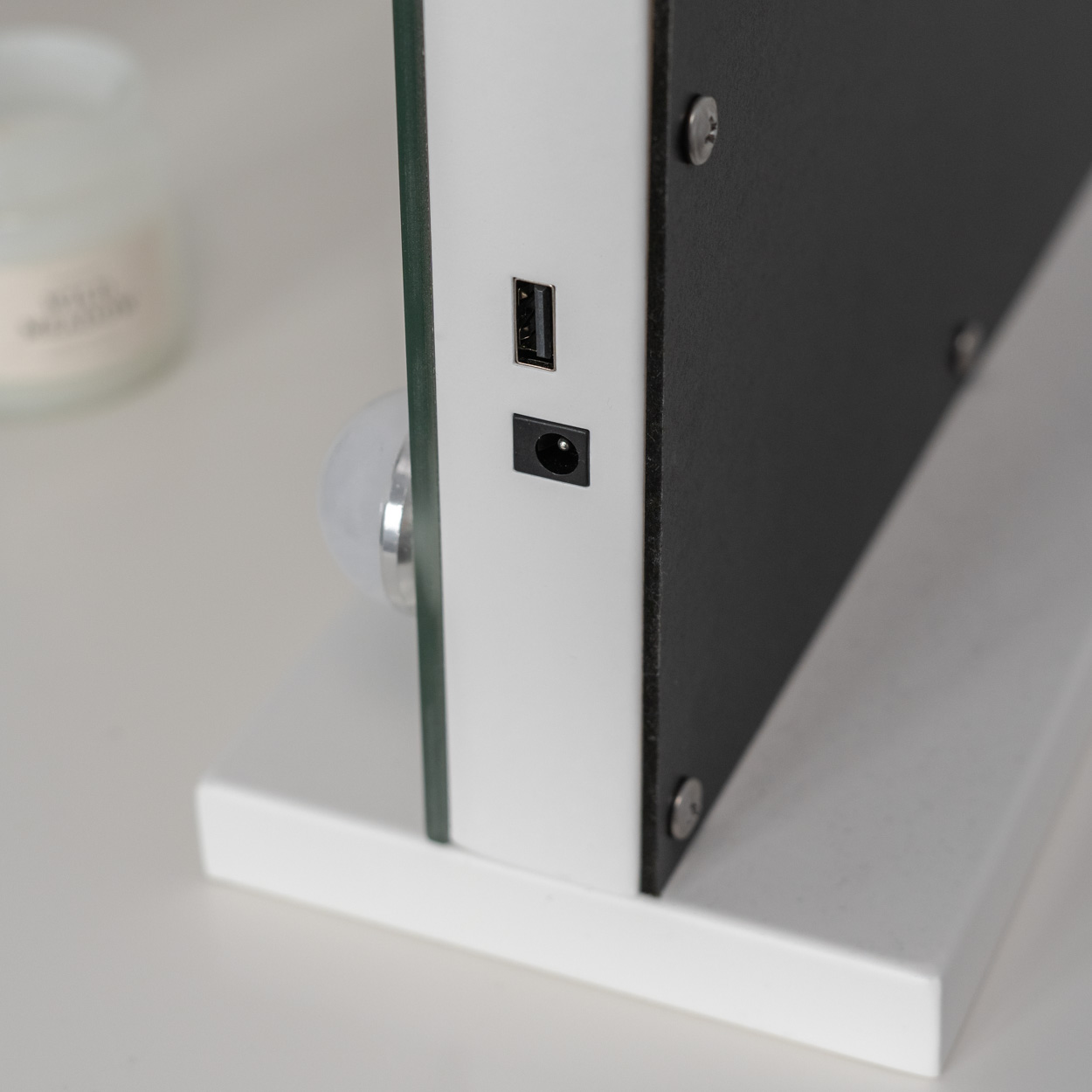 Primer plano de una base de espejo blanca. Se ven un puerto USB y un puerto de alimentación. Superficie blanca.