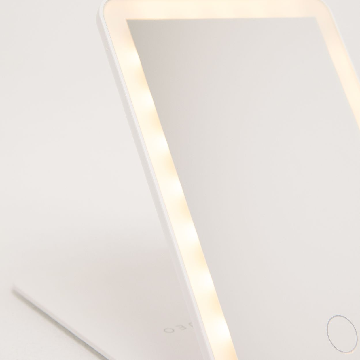 Espejo de maquillaje blanco e iluminado. Cuenta con una tira de luz integrada y un botón táctil de encendido/apagado.