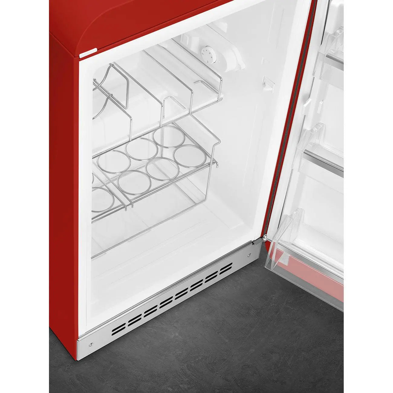 Refrigerador Smeg rojo con la puerta abierta, mostrando estantes y botellero, sobre superficie oscura.