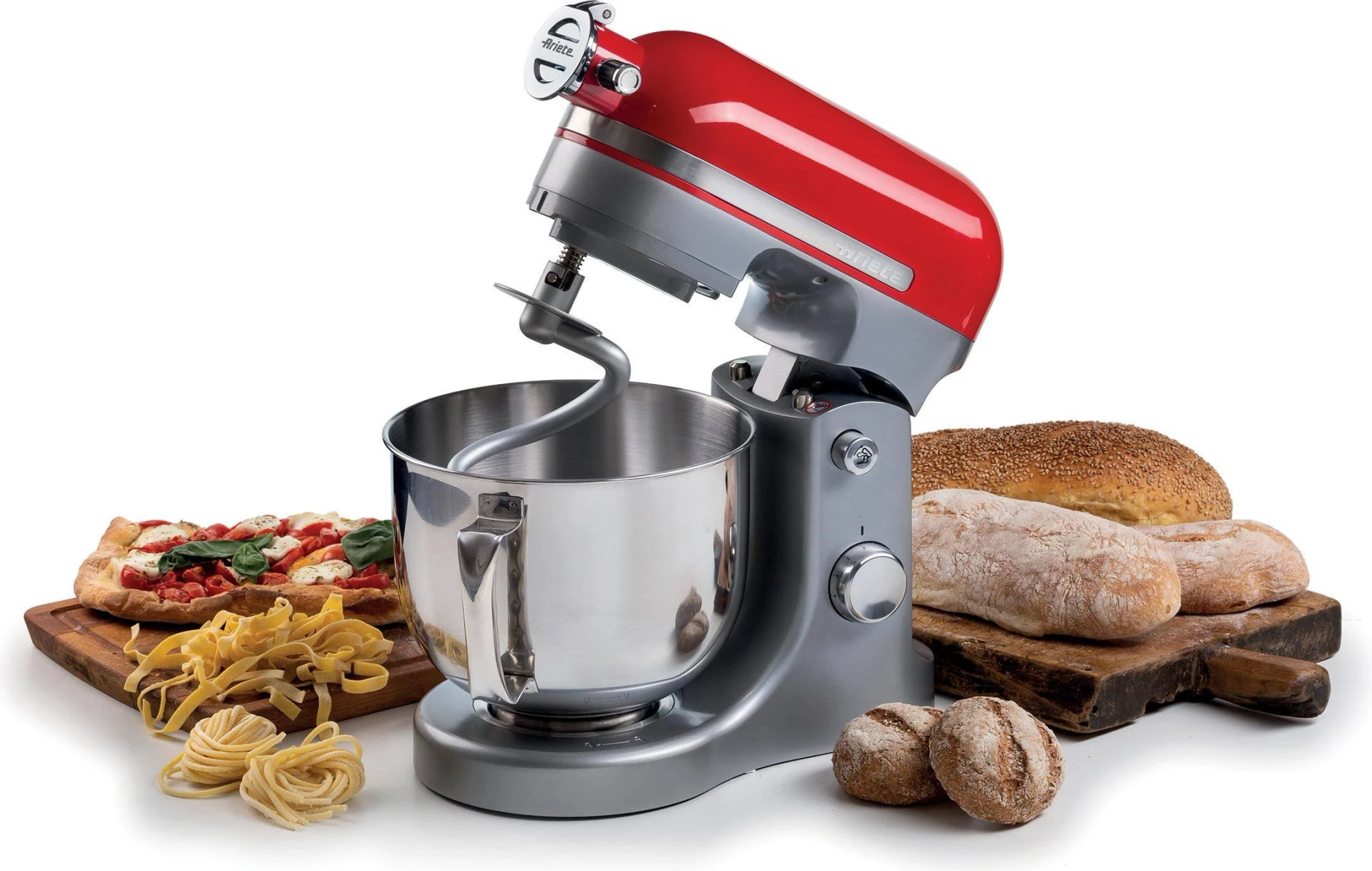 Roter Küchenmixer mit Schüssel. Brot, Pasta und Pizza auf dem Tisch. Weißer Hintergrund.