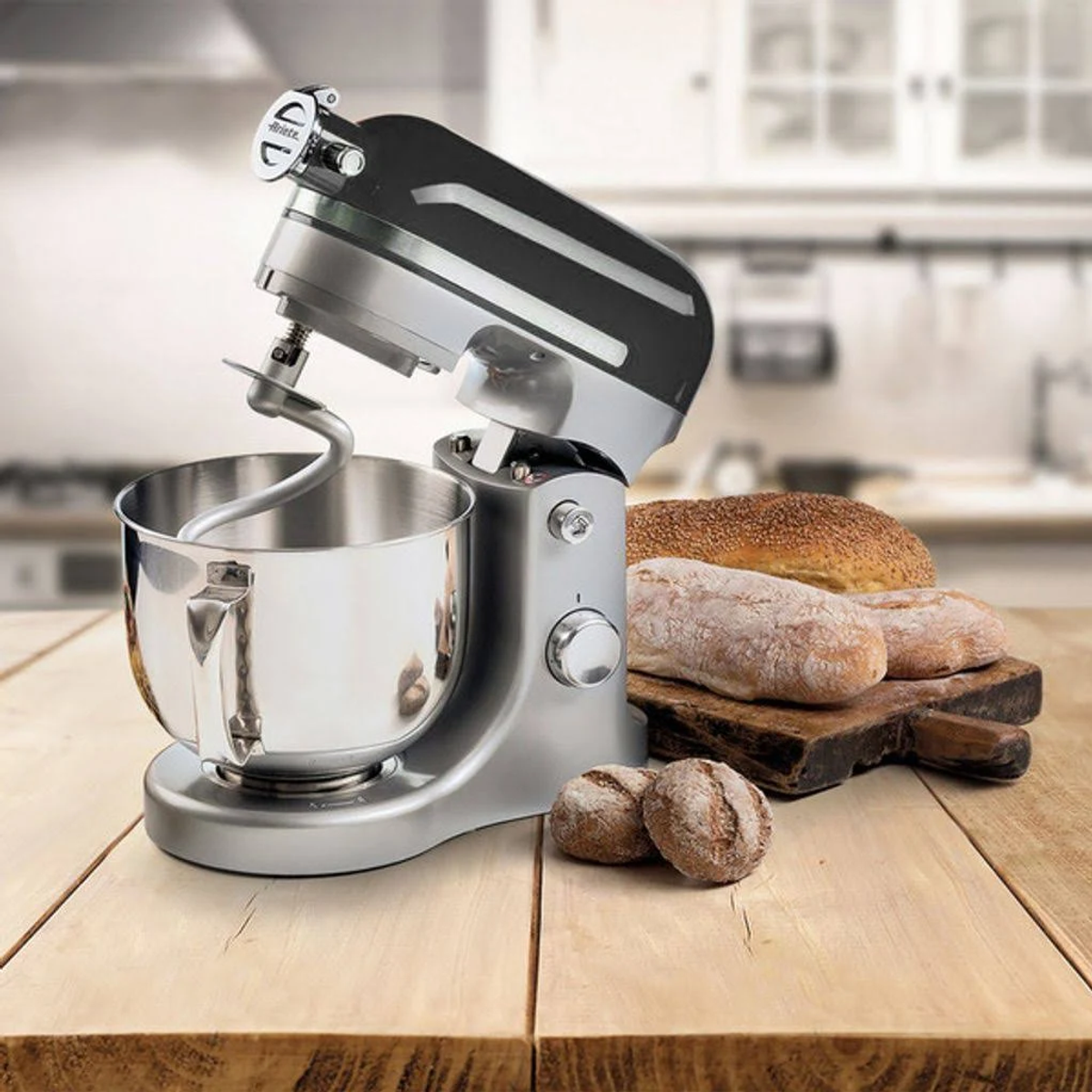Ein silberner und schwarzer Küchenmixer mit einer Rührschüssel, Brot auf einem Holzbrett.