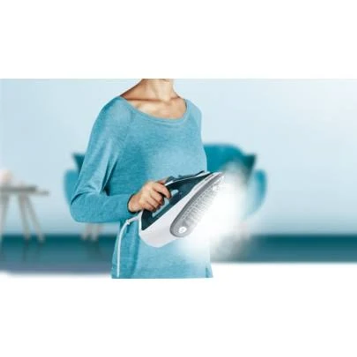 Una mujer planchando ropa. Sale vapor de la plancha. Lleva una camisa azul.