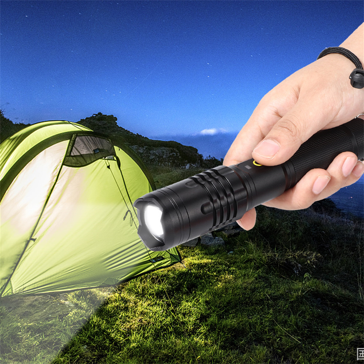 Eine Hand hält nachts eine schwarze Taschenlampe und beleuchtet ein Zelt und Gras. Der Himmel ist dunkel.