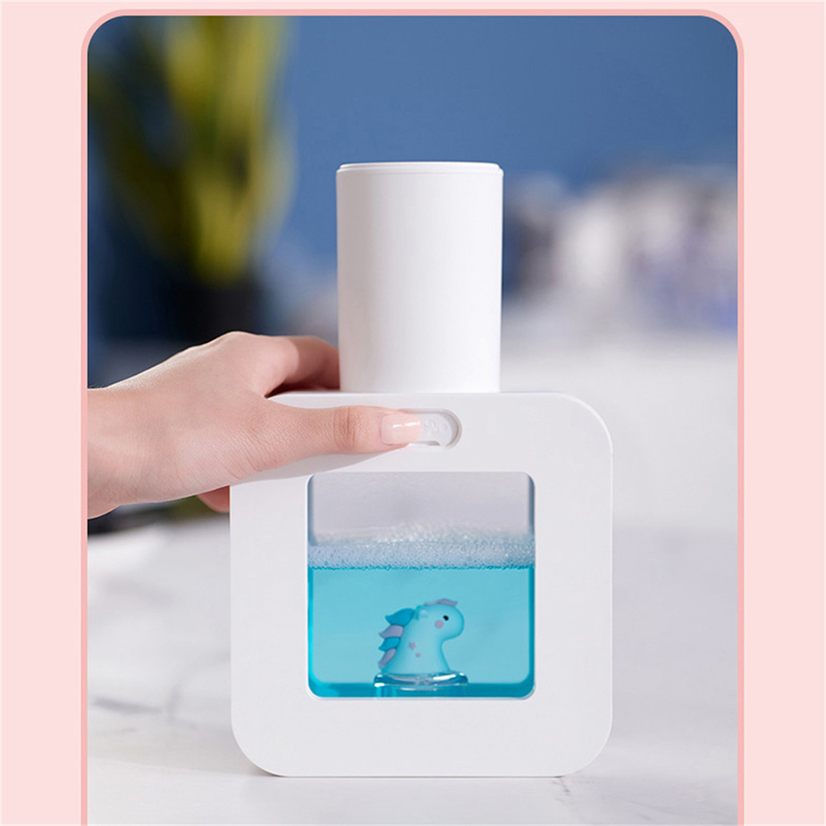 Weißer automatischer Seifenspender mit blauer Flüssigkeit und Spielzeug, rosa Hintergrund.