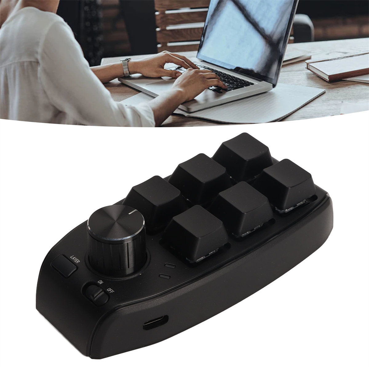 Ein schwarzes Bearbeitungsgerät mit Knöpfen und Tasten, in der Nähe eines Laptops und einer tippenden Person.