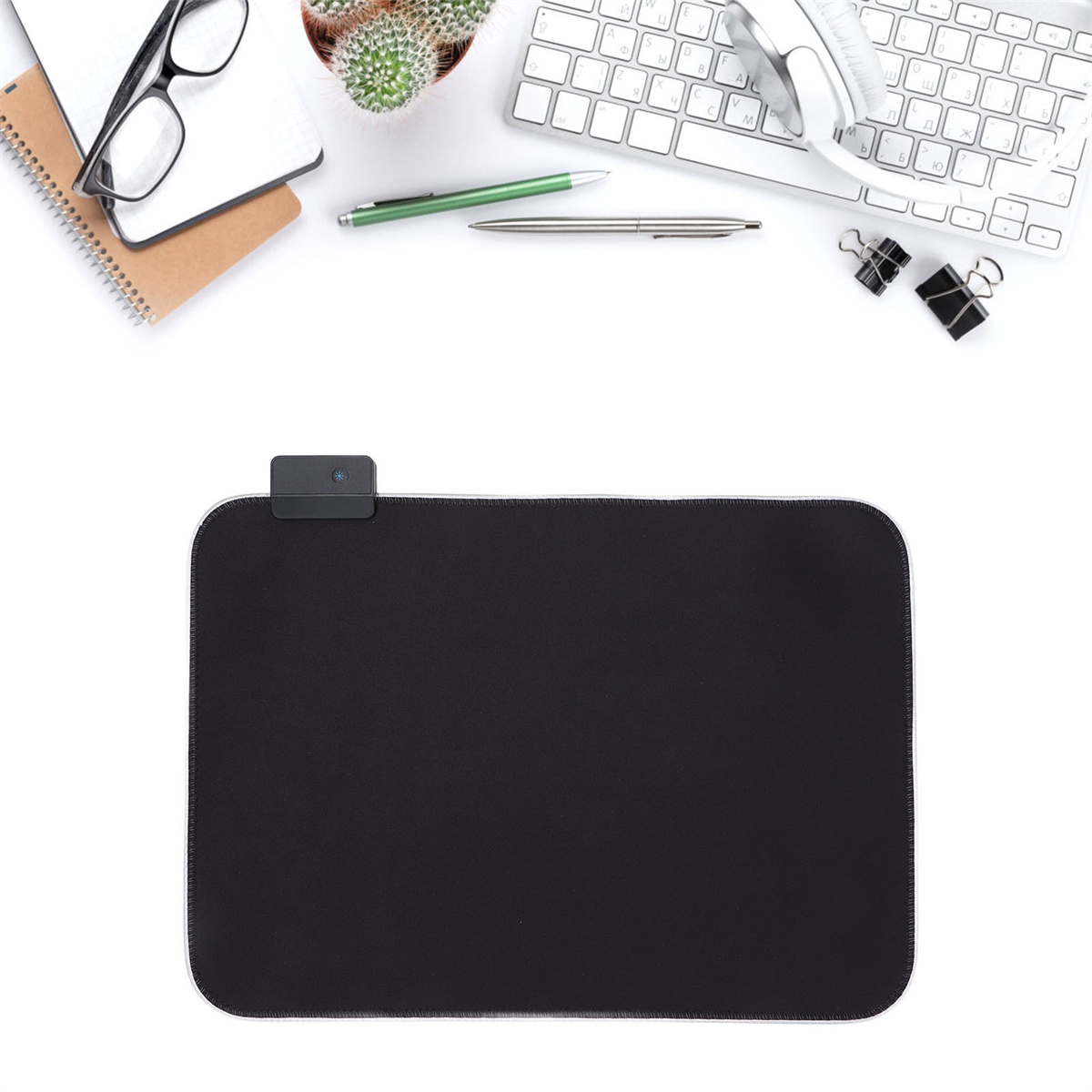 Draufsicht auf einen Schreibtisch mit Mauspad, Tastatur, Brille, Notizblock, Stift und Kopfhörern.