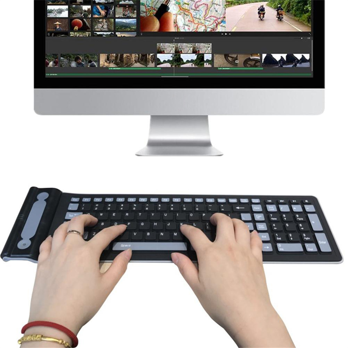 Hände tippen auf einer schwarzen Tastatur, im Hintergrund ein Computer mit Videoschnittsoftware.