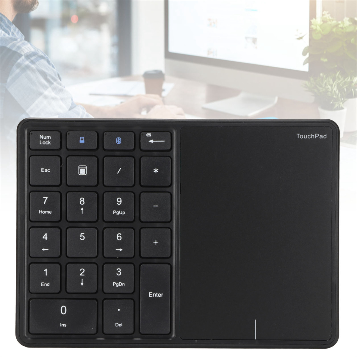 Schwarzer Ziffernblock und Touchpad. Die Hand einer Person ist unscharf. Computermonitor im Hintergrund.