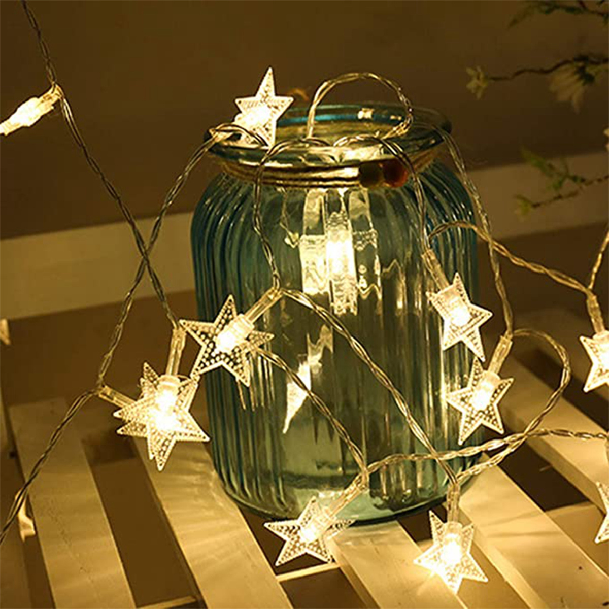 Lichterkette mit sternförmigen Lichtern vor einem blauen, geriffelten Glasgefäß auf Holz.