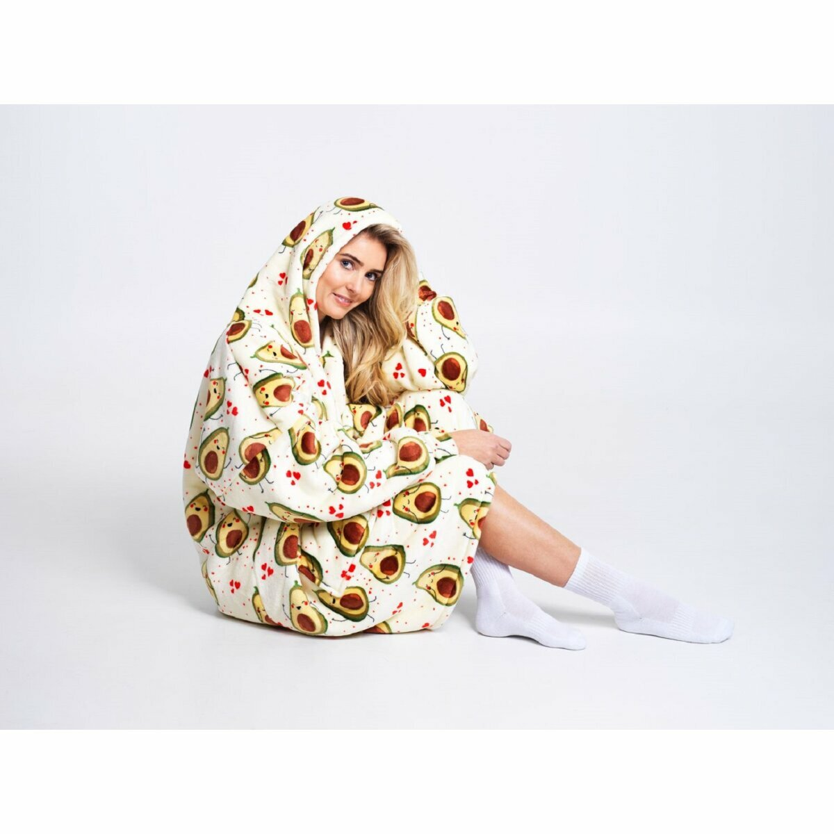 Eine Frau in einem Hoodie mit Avocadomuster sitzt lächelnd auf dem Boden, mit weißen Socken.