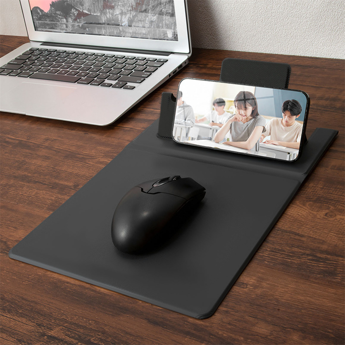 Laptop, Maus und ein Telefon, das ein Video auf einem Pad auf einem Holzschreibtisch anzeigt.