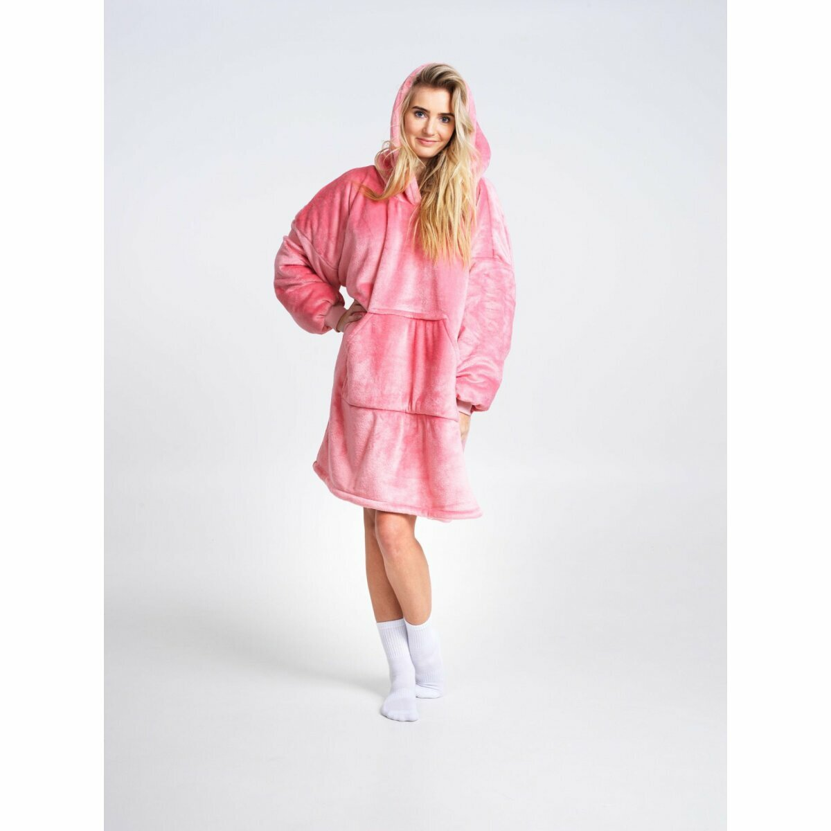 Eine Frau trägt einen rosa Hoodie. Sie hat blondes Haar und lächelt. Der Hintergrund ist weiß.