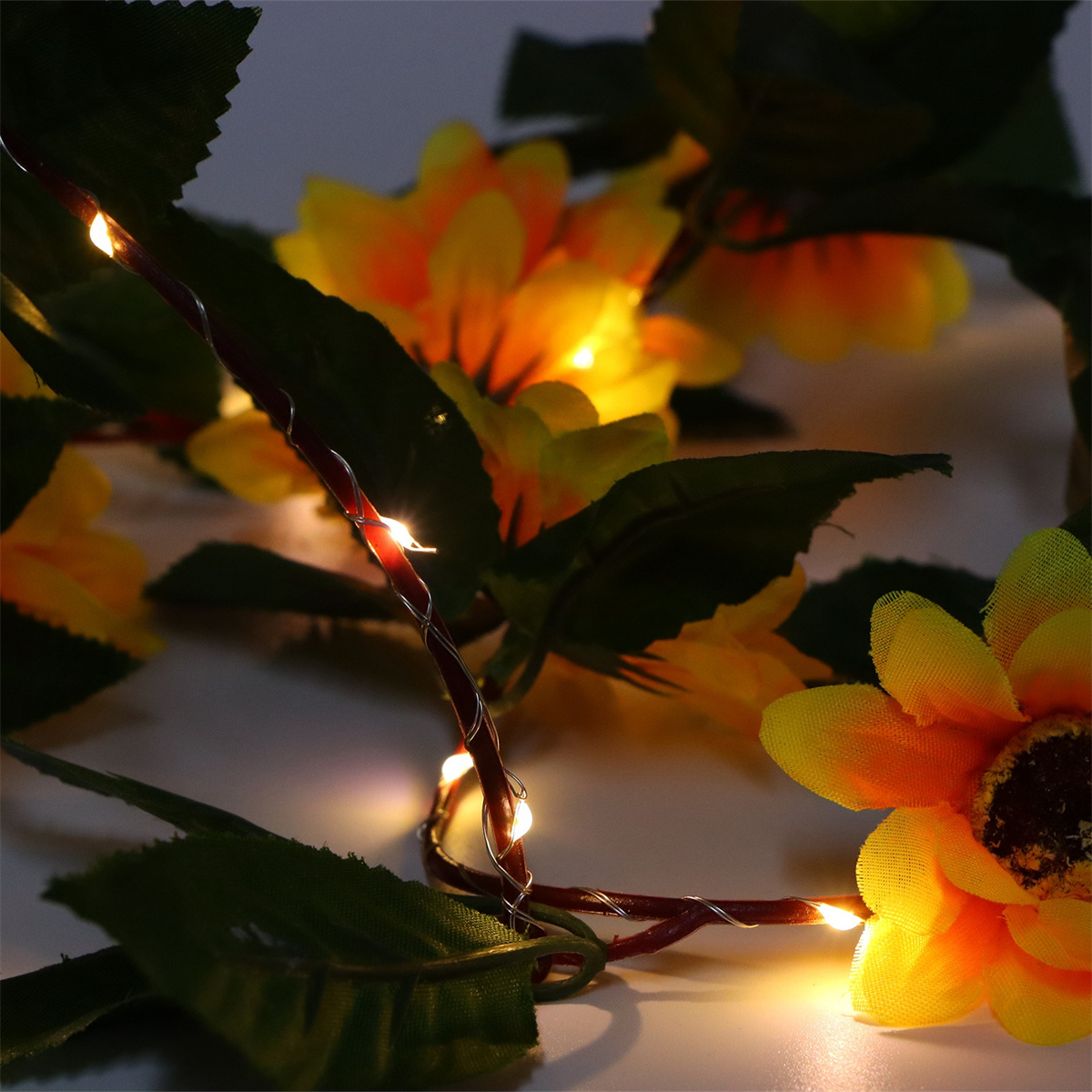 Nahaufnahme von Sonnenblumen und Lichterketten. Die Lichter sind an und beleuchten die Blumen. Dunkler Hintergrund.
