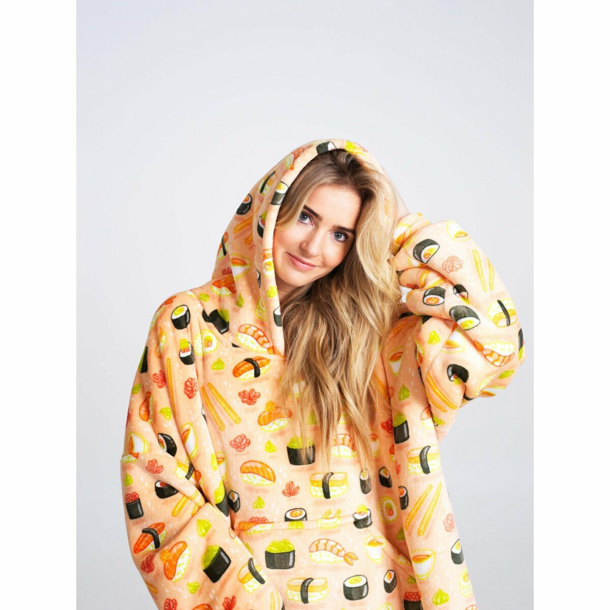 Eine Frau in einem Kapuzenpullover mit Sushidruck lächelt. Der Kapuzenpullover ist pfirsichfarben mit Sushi-Illustrationen.
