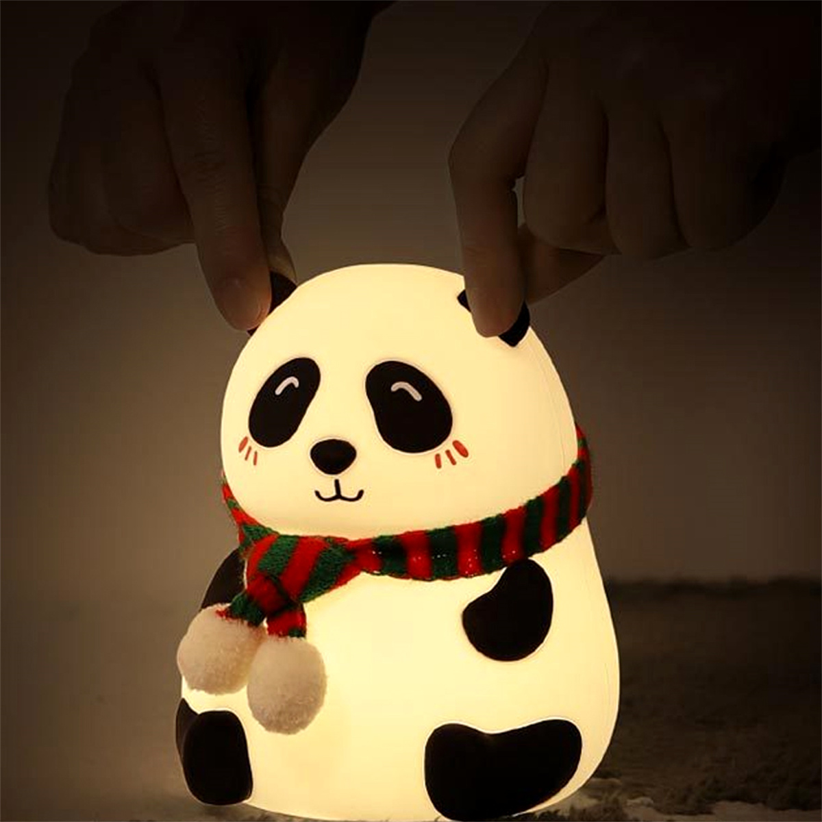 Ein Panda-Nachtlicht mit schwarzen Ohren, Augen und einem Schal wird von zwei Händen gehalten.
