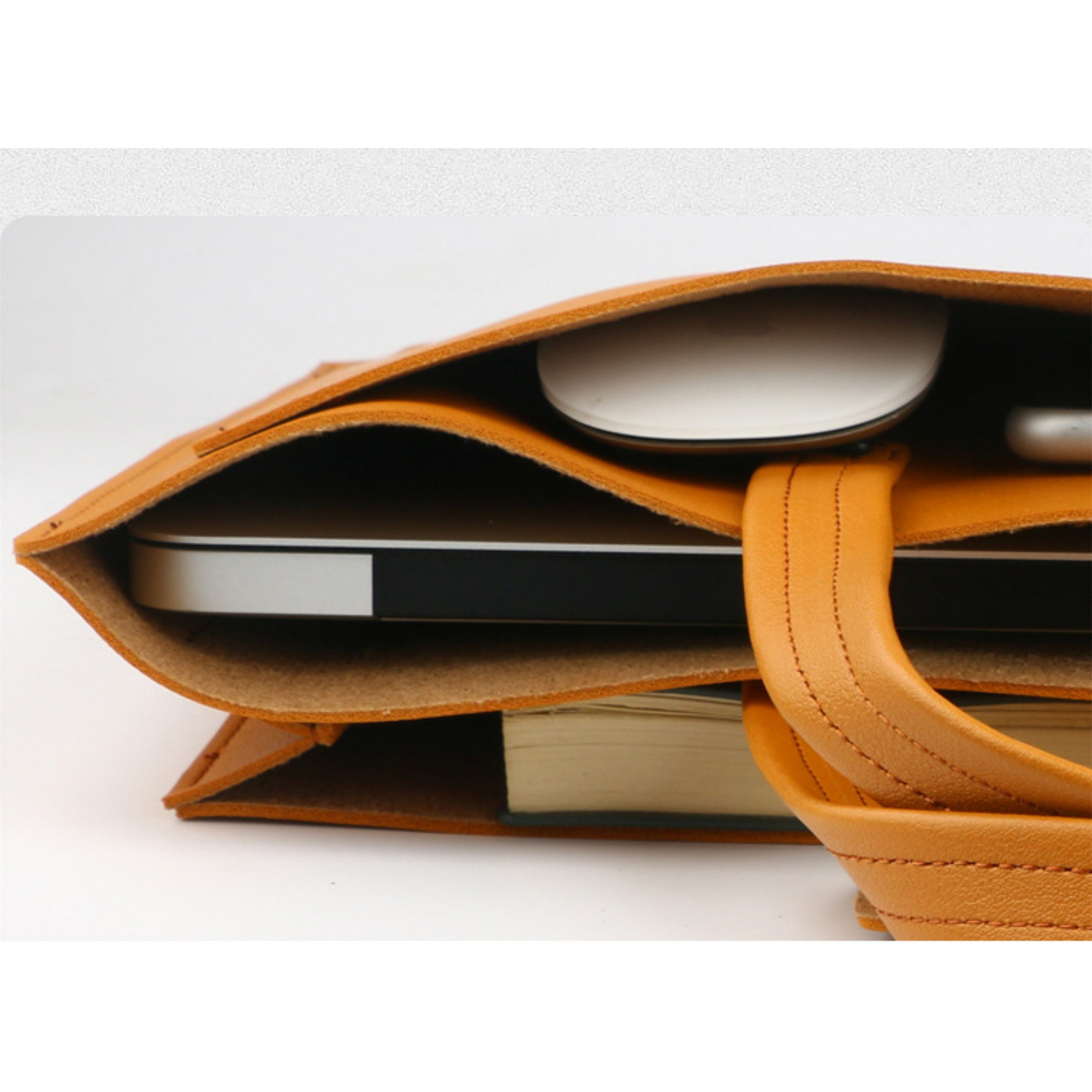 Offene braune Ledertasche mit Laptop, Buch und Maus. Beiger Hintergrund.