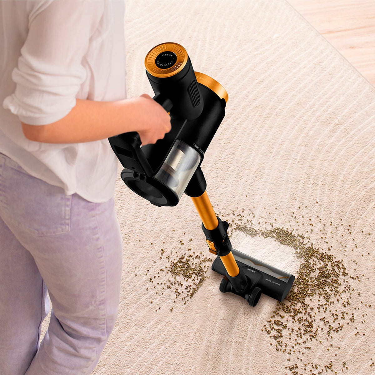 Persona usando una aspiradora negra y dorada sobre una alfombra beige con residuos. La persona usa jeans.