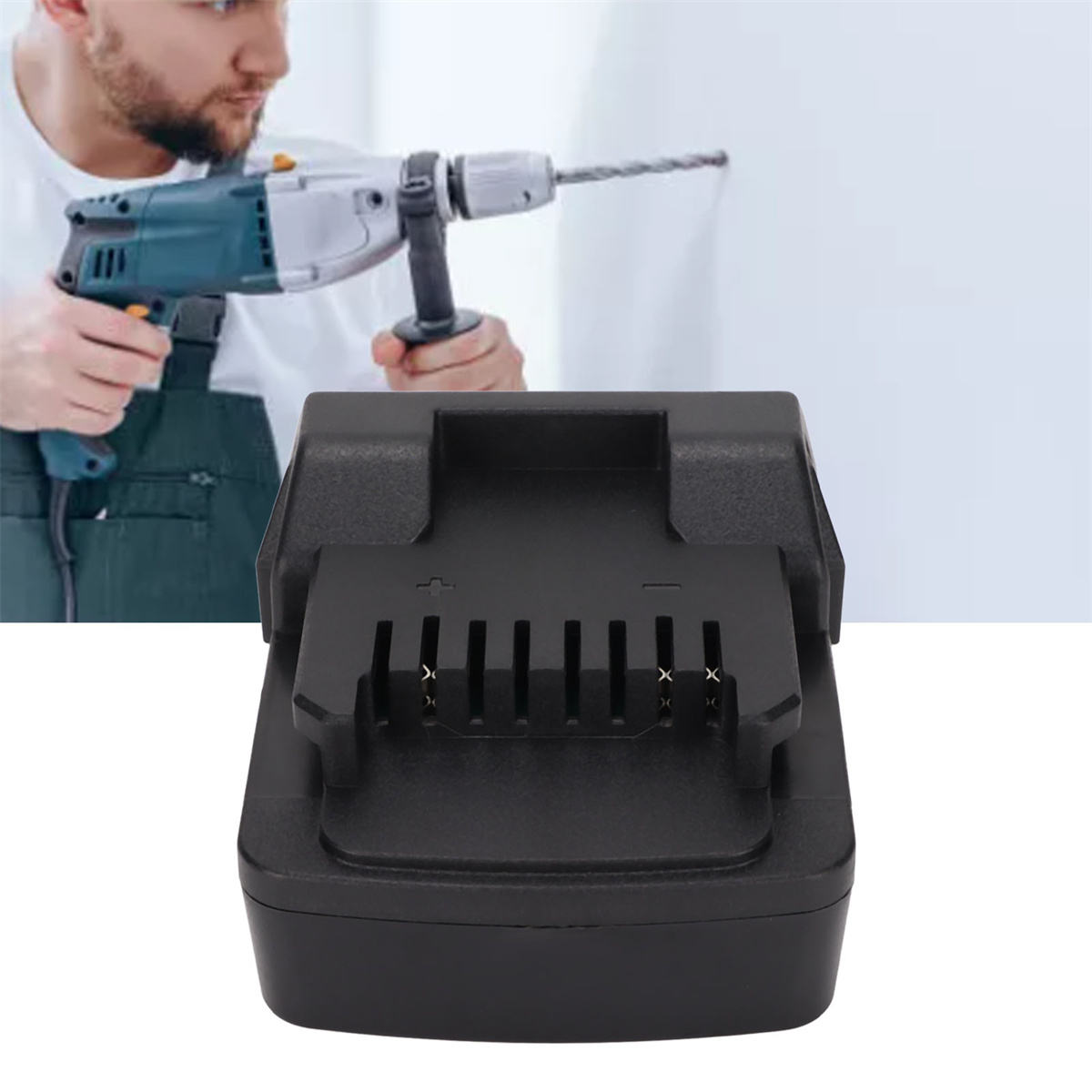 Schwarzes Ladegerät im Fokus; Person mit Bohrmaschine im Hintergrund. Weiße Wand.