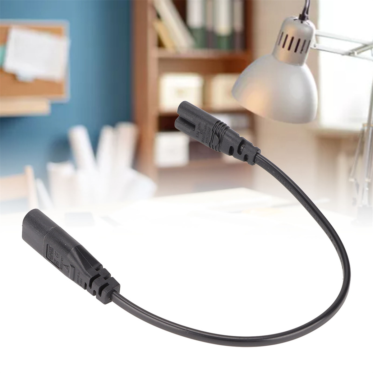 Schwarzes Netzkabel mit zwei Steckern. Im Hintergrund eine Lampe und ein Schreibtisch.