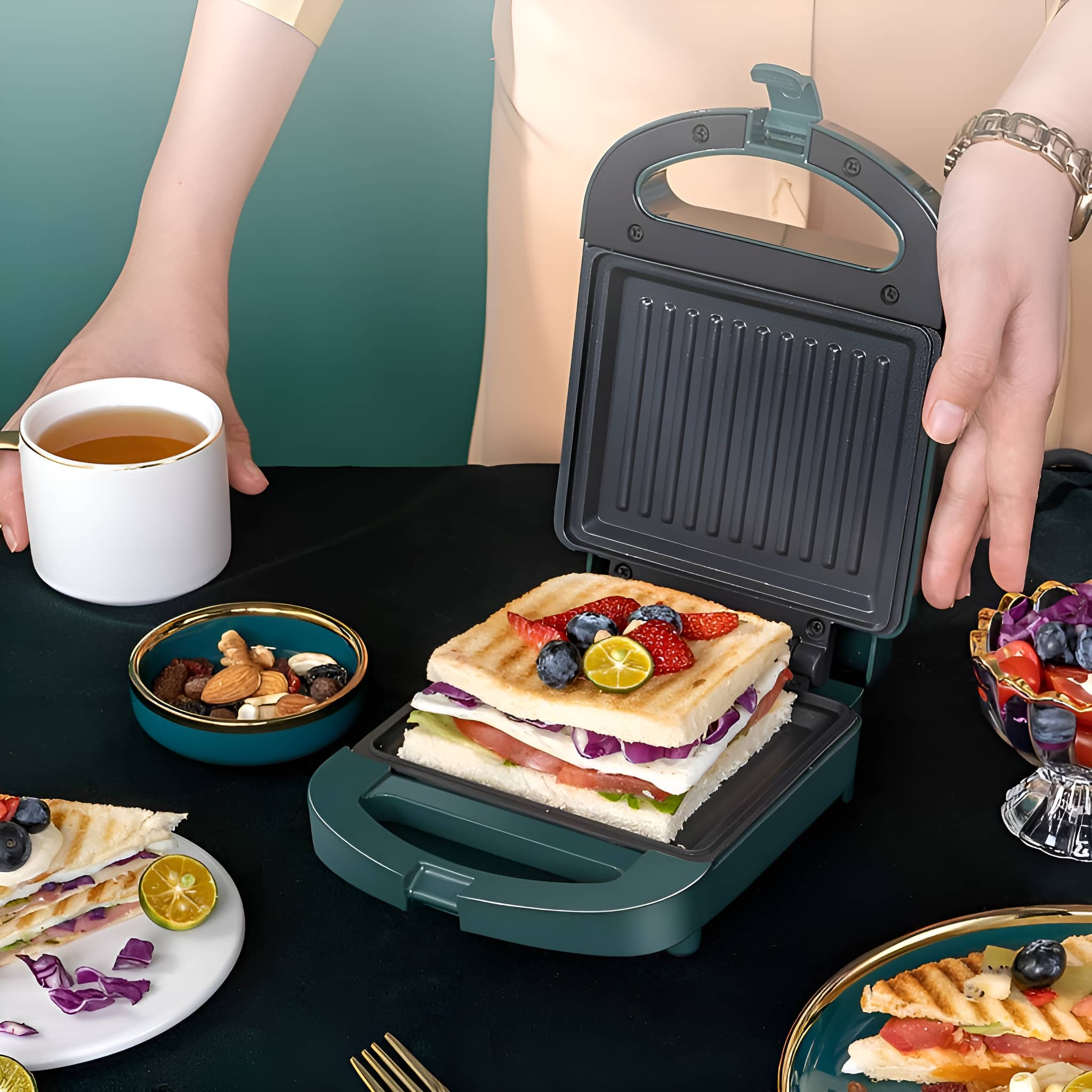 Sandwichmaker mit Sandwich. Tee, Nüsse und Früchte sind auf dem Tisch.