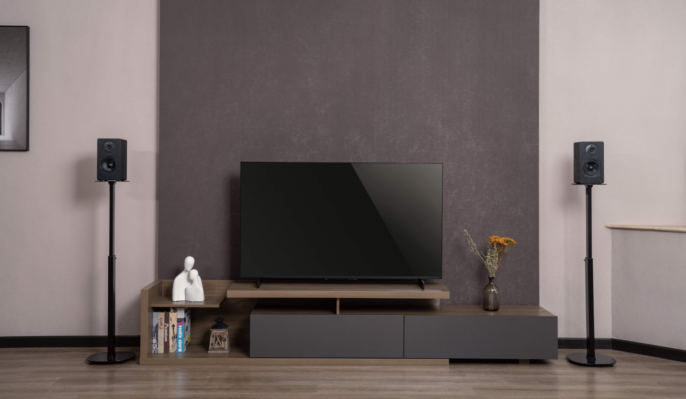 Woonkamer met tv op een standaard, twee luidsprekers op standaards en decoratie. Bruin- en grijskleurenschema.