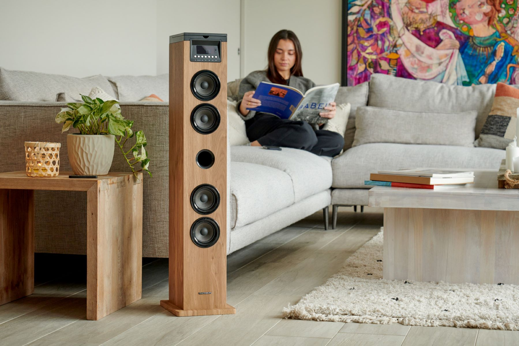 Wysoki drewniany głośnik z kobietą czytającą książkę na sofie w dobrze oświetlonym salonie.