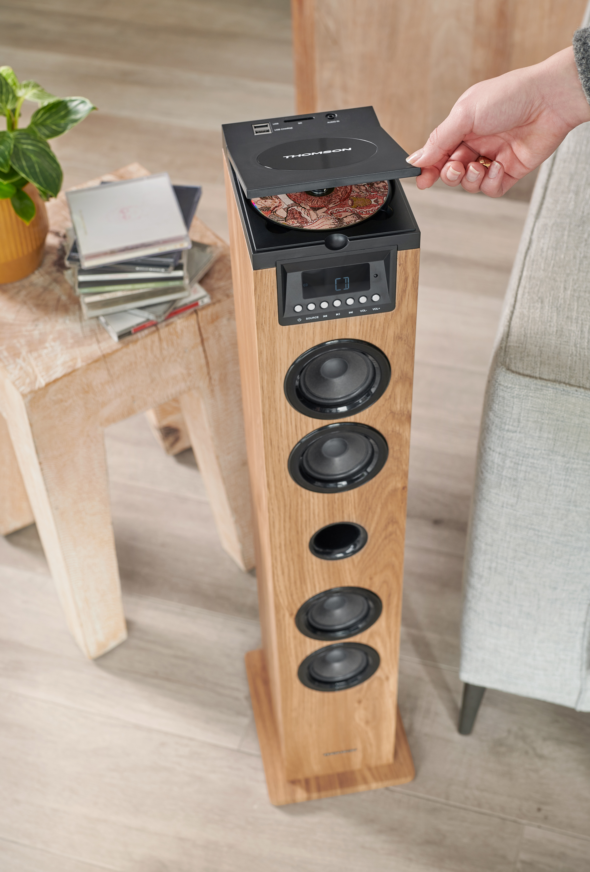 Drewniany głośnik z odtwarzaczem CD. Ręka otwiera tacę, aby włożyć płytę CD.